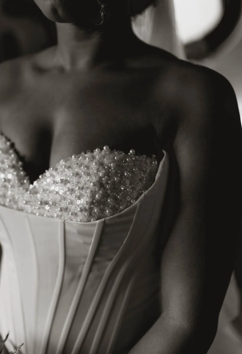 Close-up of a woman in a strapless dress with beaded embellishments, showing her shoulders and upper chest in black and white.