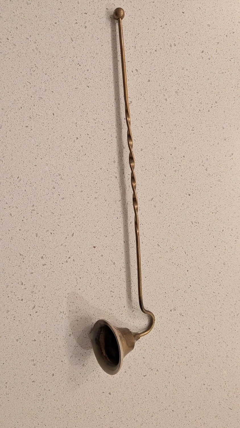 A brass candle extinguisher lies on a polished white granite countertop.