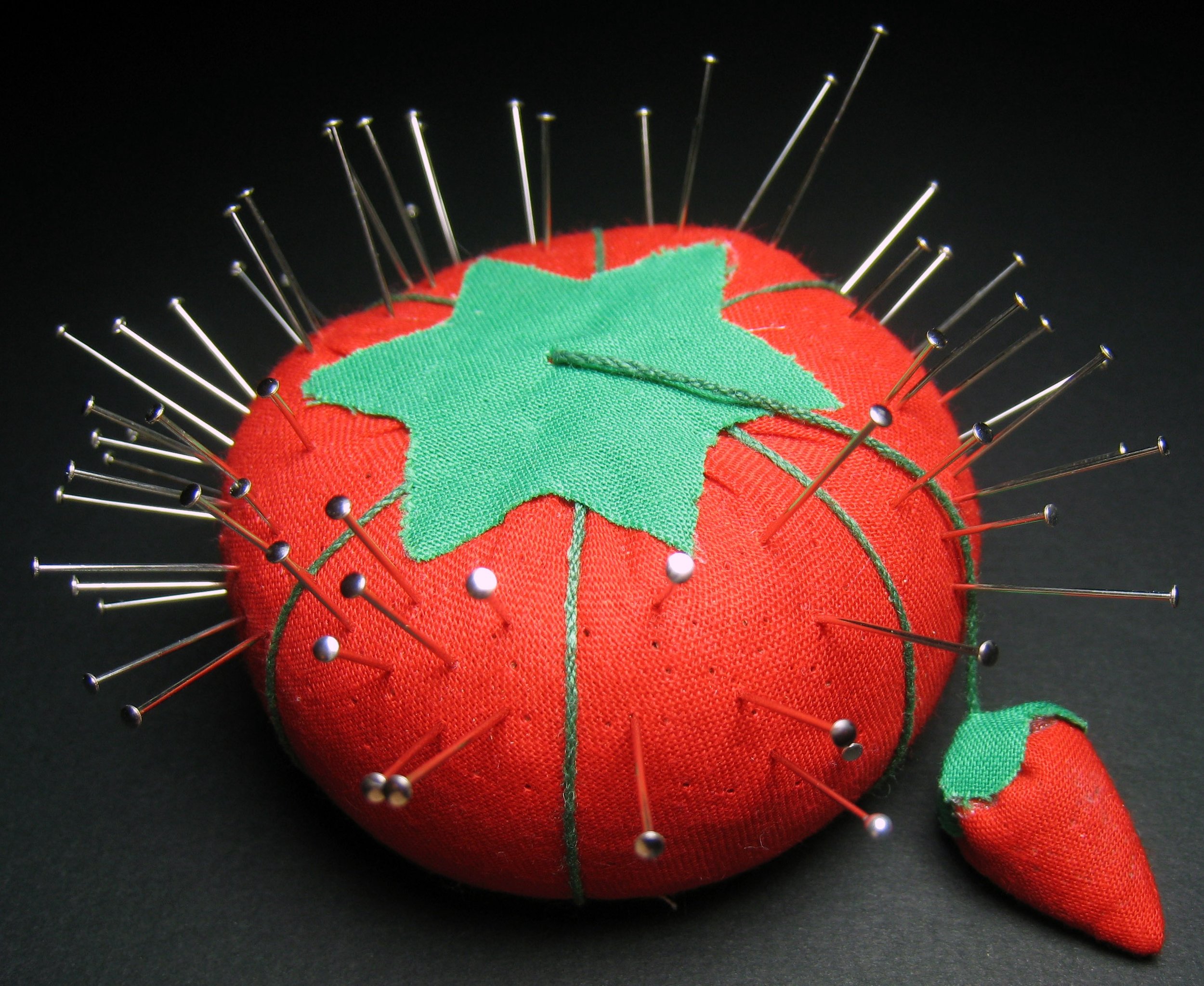 Close-up photo of a pincushion in the shape of a strawberry, stuck with many steel-coloured pins.