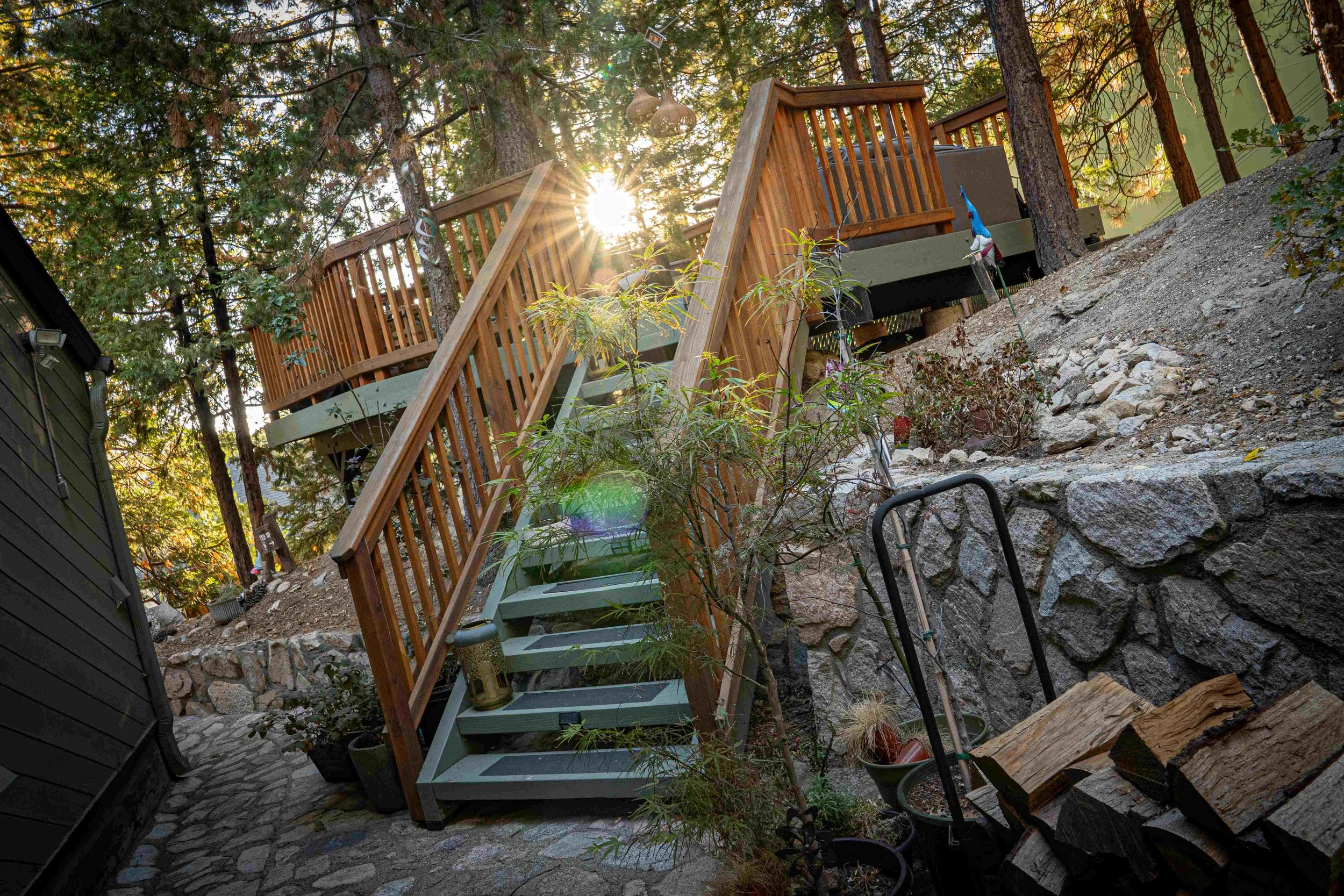 Sun shining through trees illuminating a wooden staircase leading up to a deck in a wooded backyard.