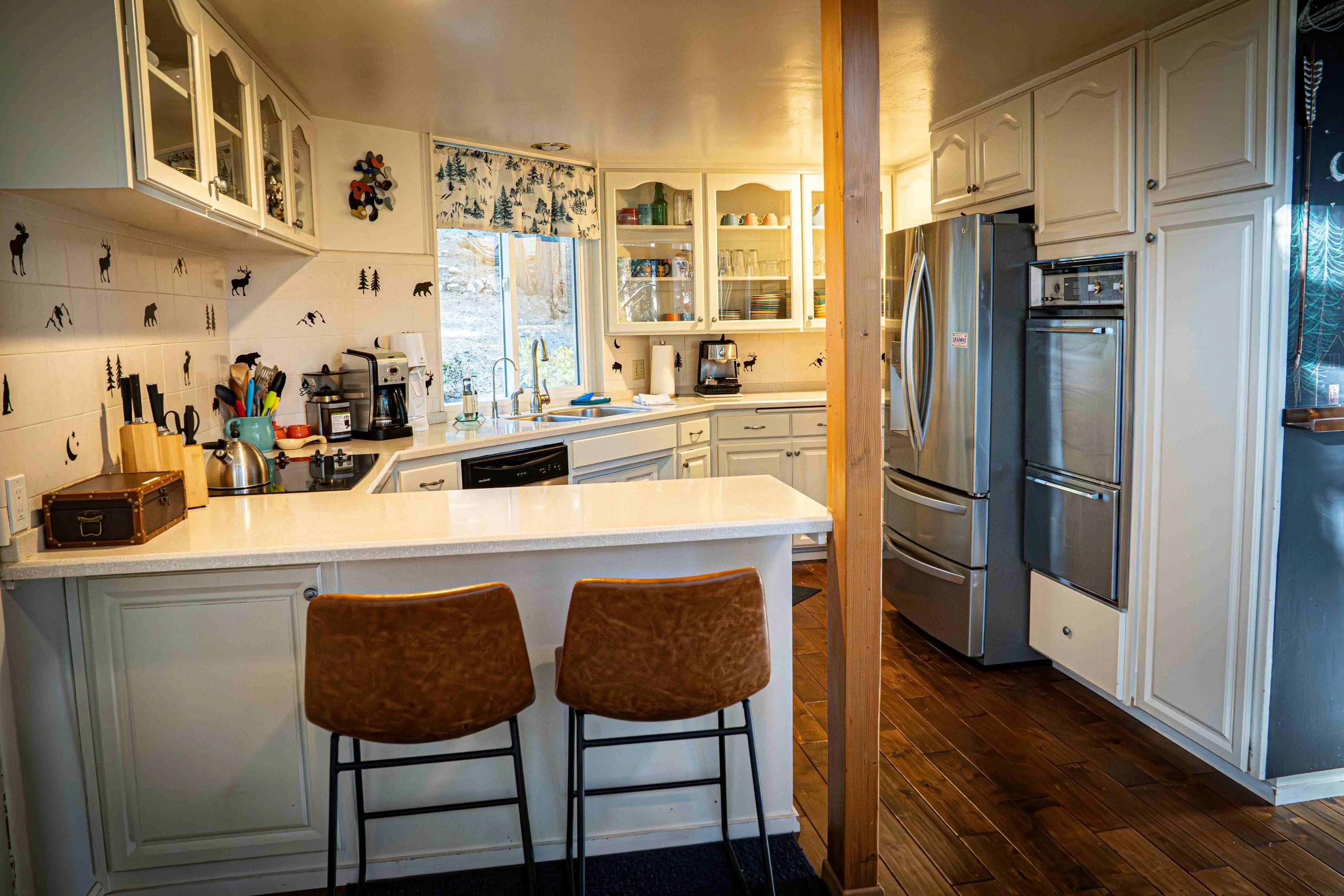 Kitchen with white cabinets, wooden floors, stainless steel refrigerator, and a white island with two brown chairs.