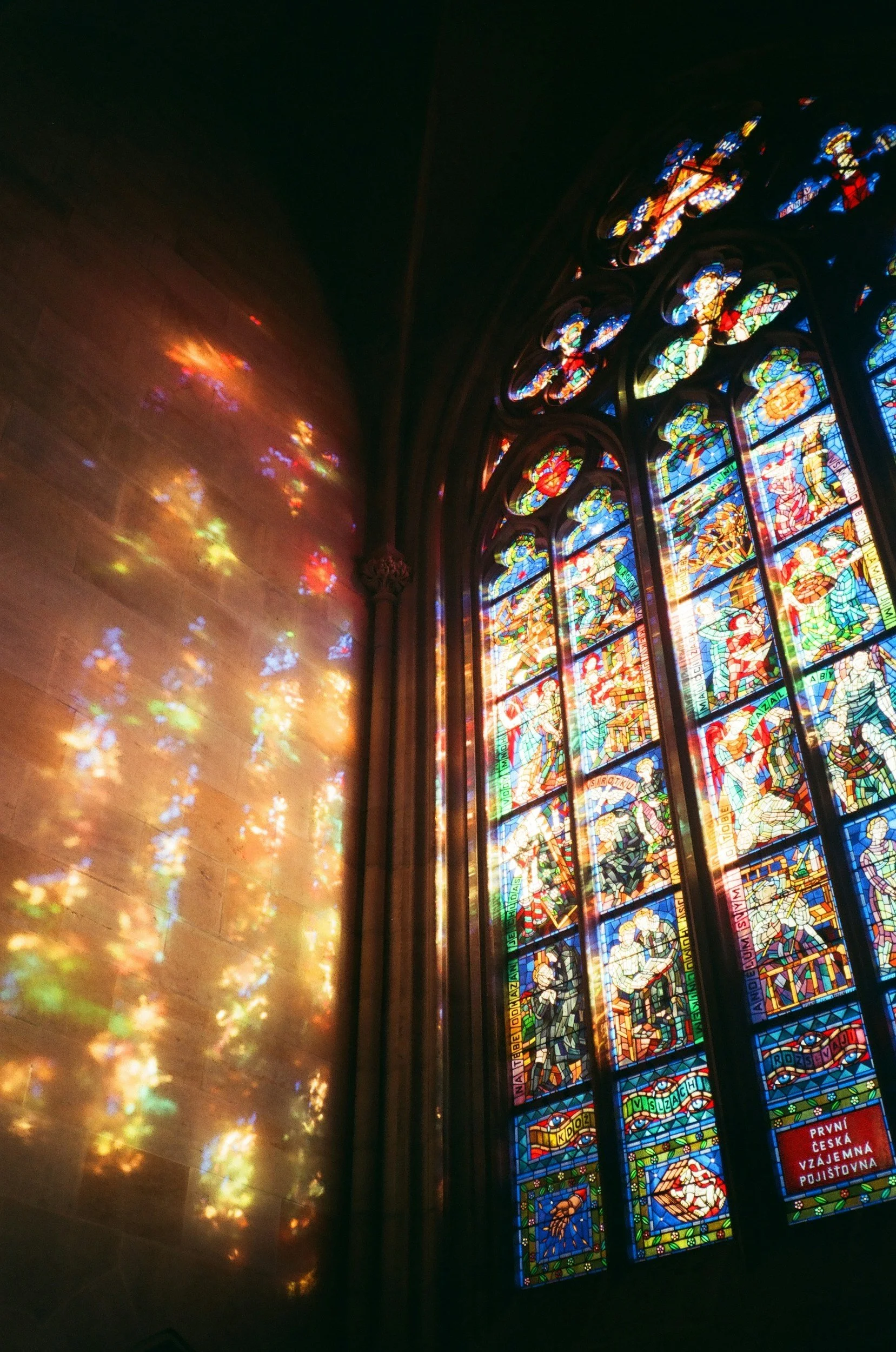 Colorful stained glass window with sunlight creating multi-colored reflections on the wall inside a church.