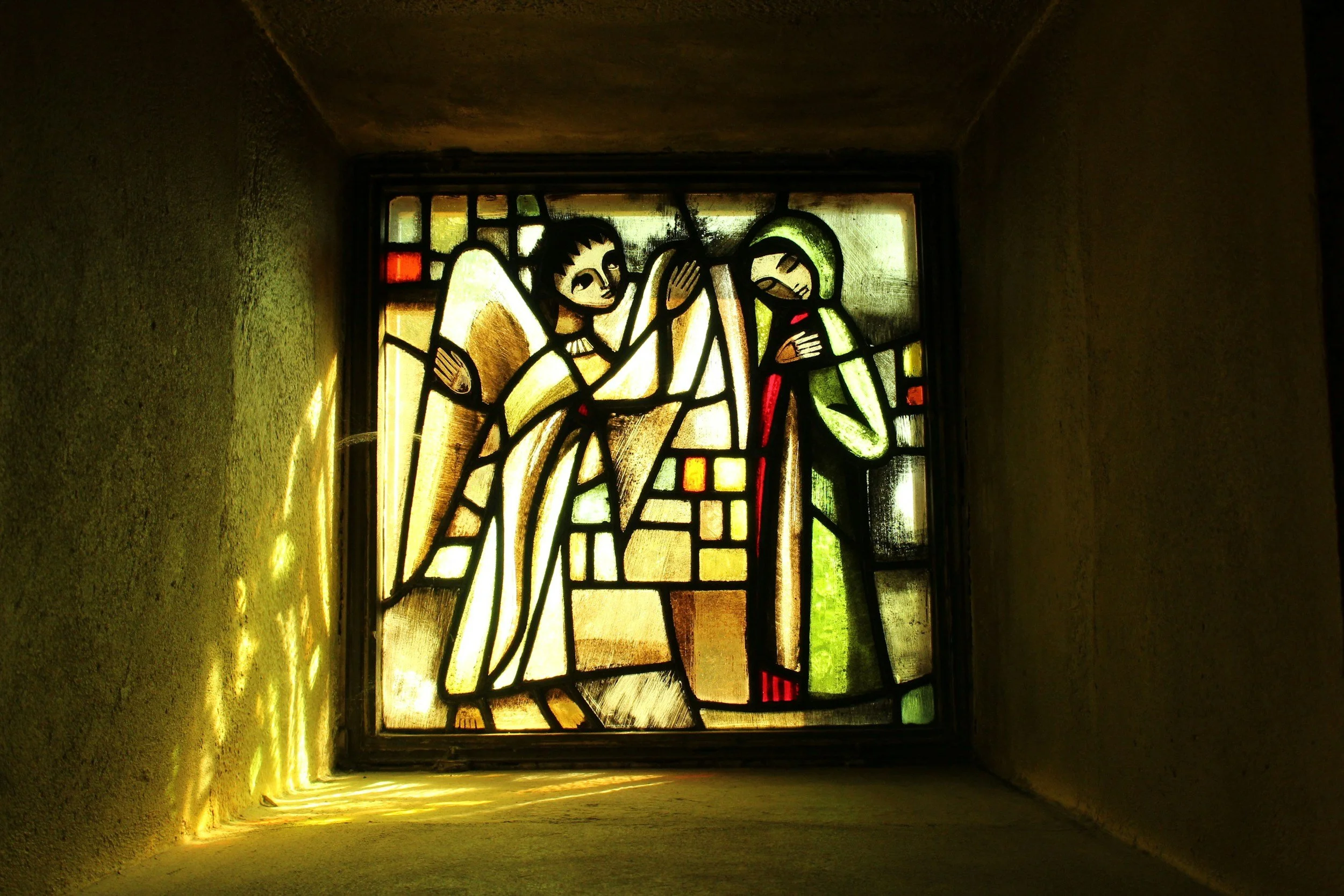 Stained glass window depicting a biblical scene with two angelic figures and a woman with a halo.