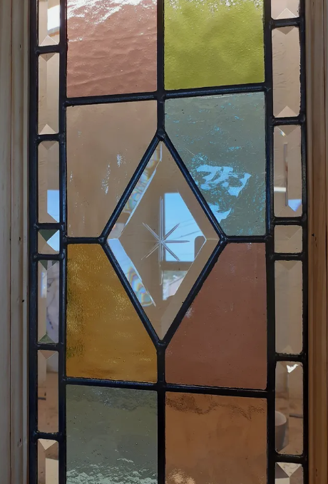 Colorful stained glass window with a diamond-shaped clear central pane and a geometric pattern.