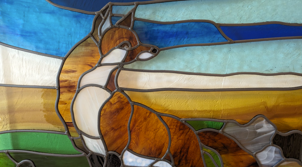 Close-up of a stained glass window depicting a horse with a blue sky background.