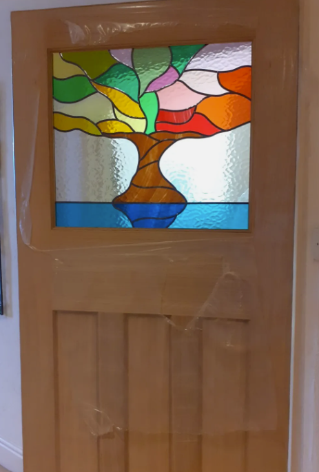 Wooden door with a stained glass window depicting a stylized tree with multicolored leaves.