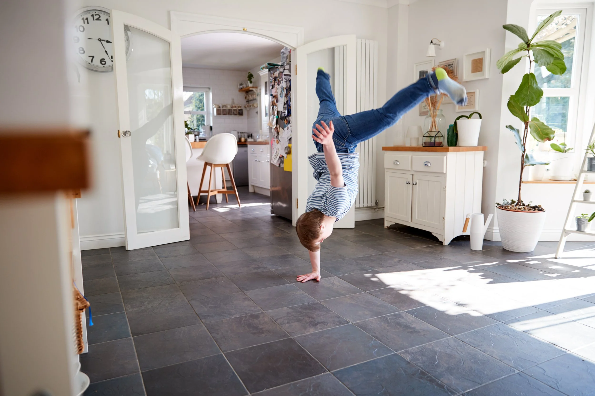 Young child smiling while learning hip hop dance moves in a kitchen at home
