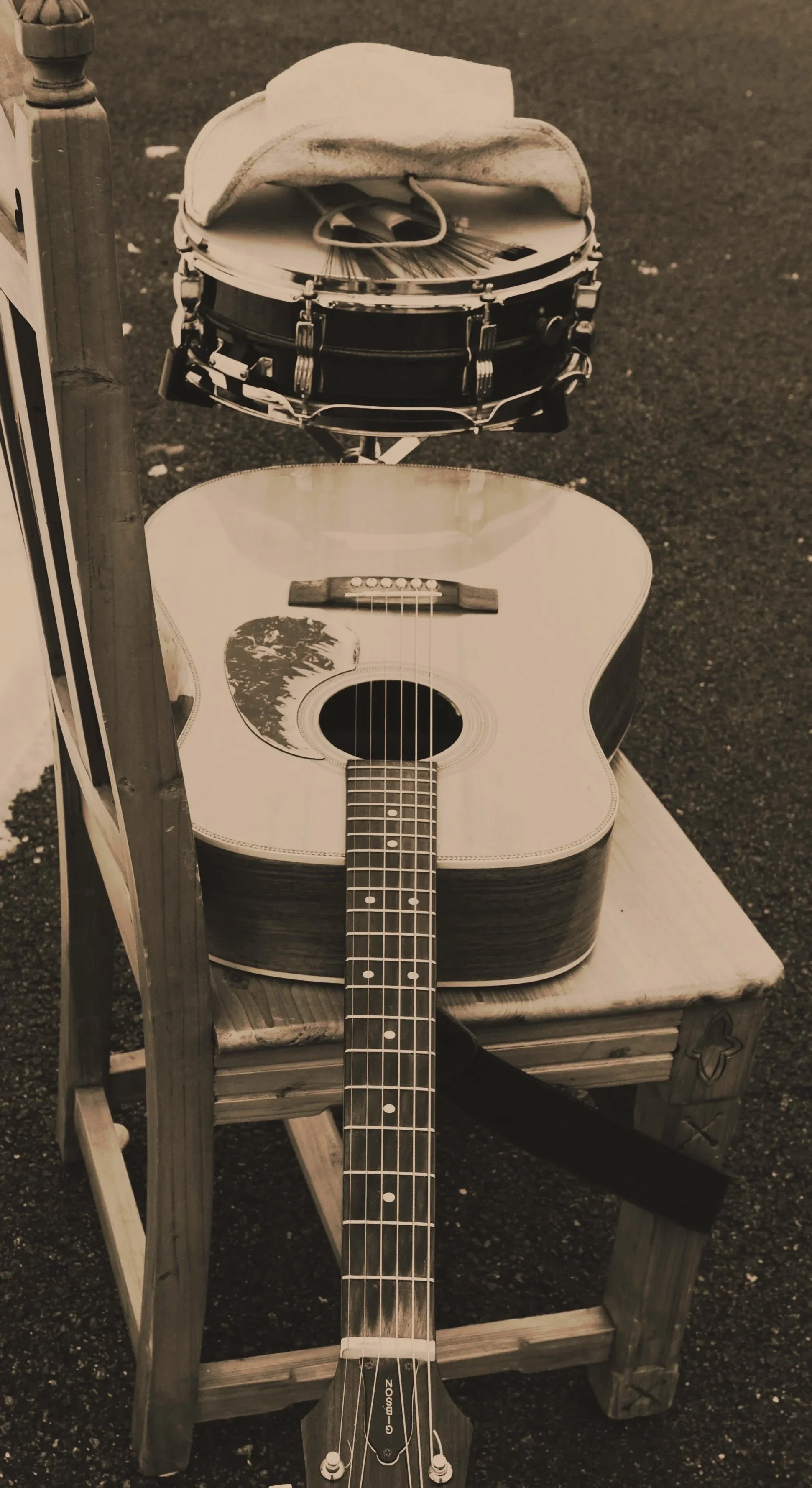 An acoustic guitar resting on a wooden chair with a small drum and a hat on top of it.