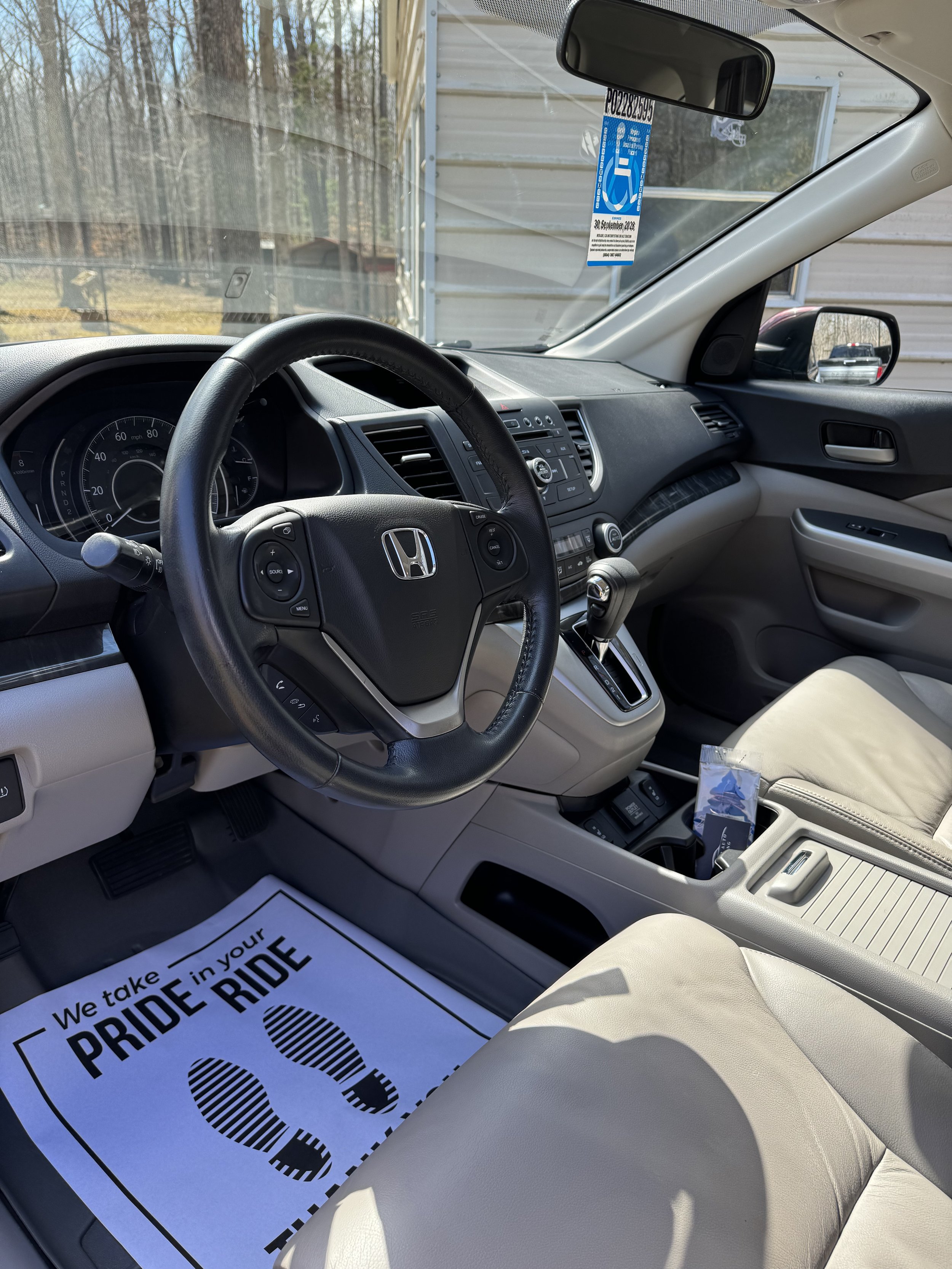 Interior of a Honda vehicle showing the steering wheel, dashboard, gear shift, and front seats with a paper floor mat that reads "We take PRIDE in your RIDE".