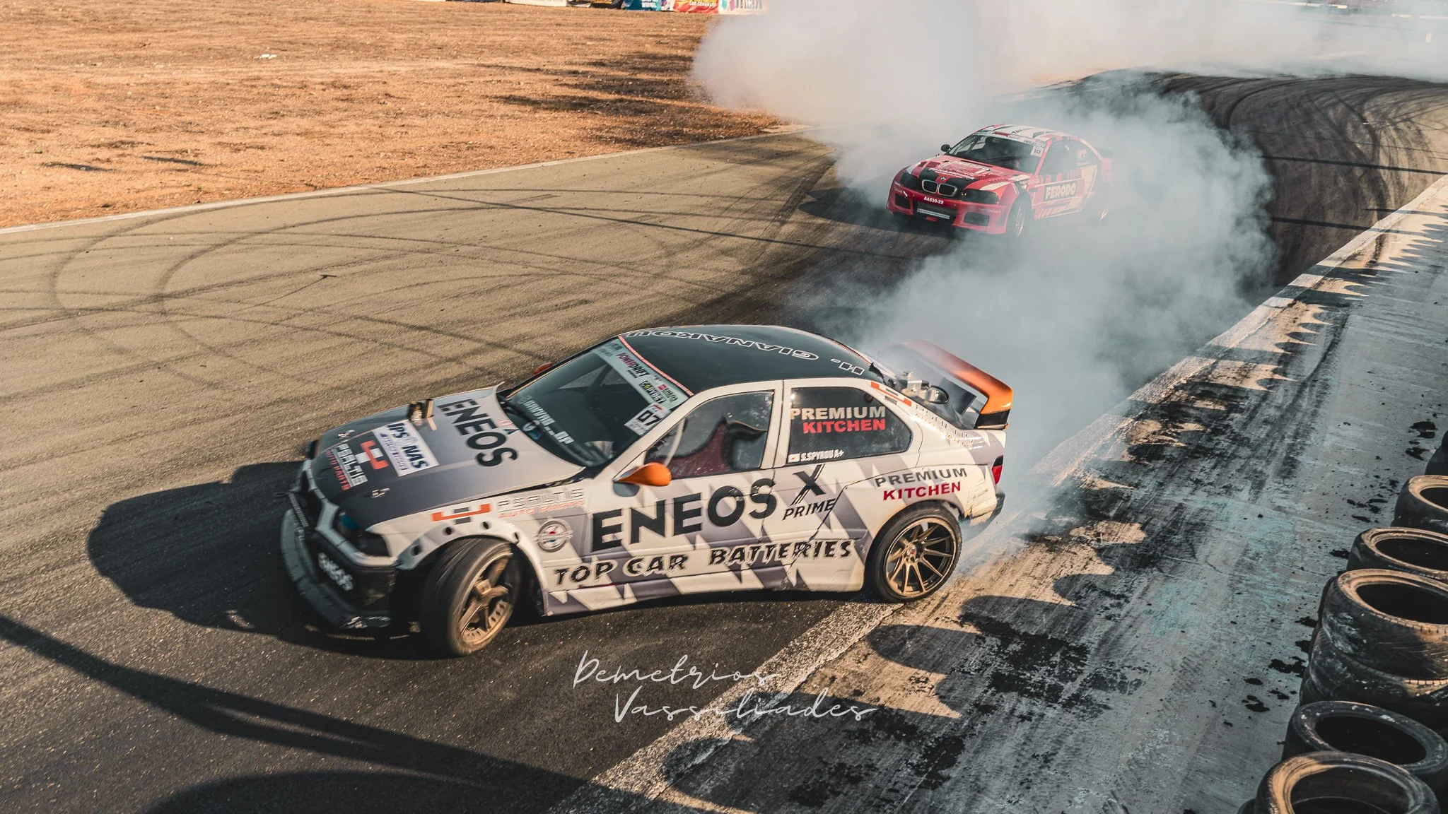 White Grey ENEOS-sponsored drift car drifting with another car chasing closely behind.