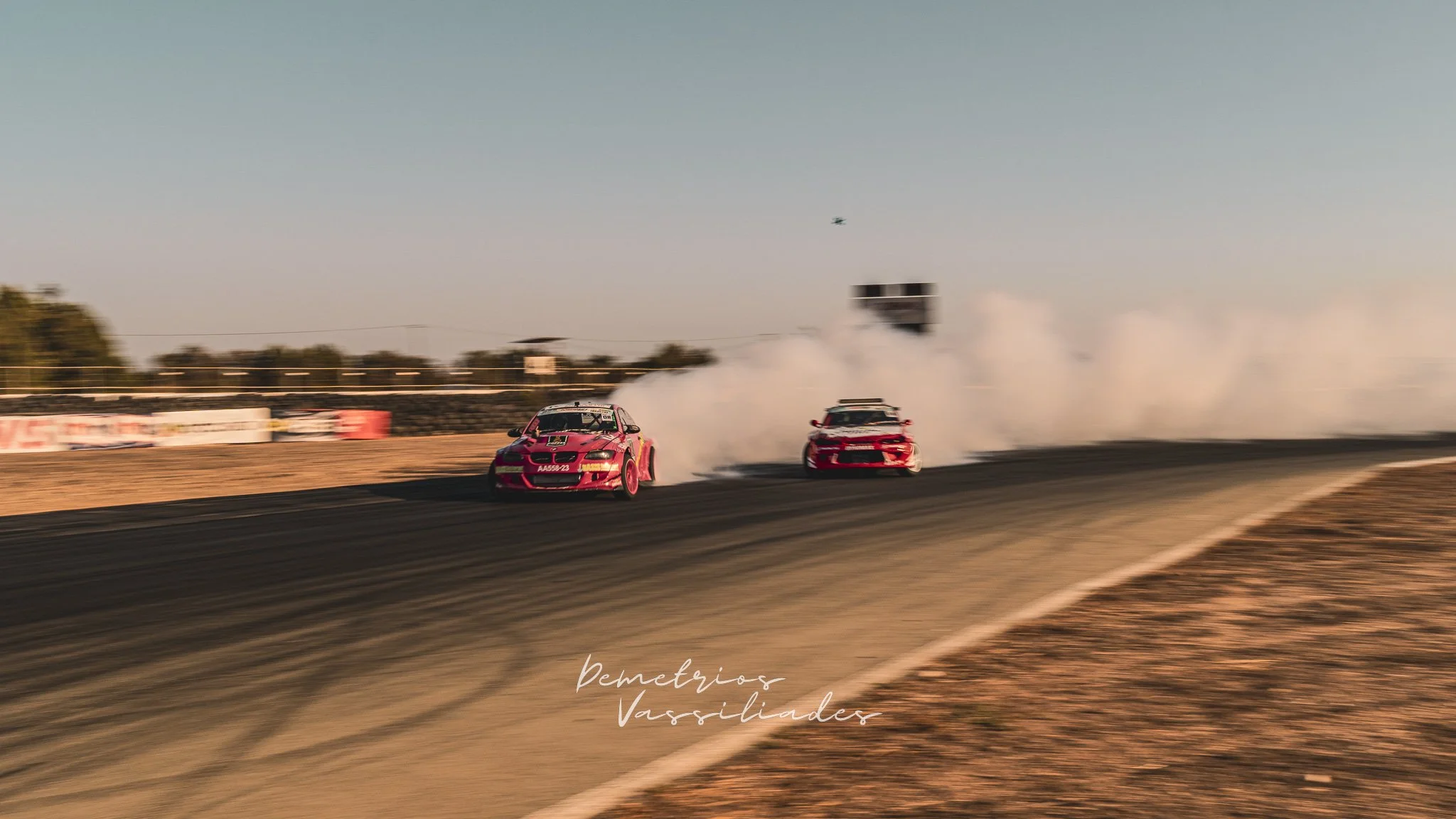 Two red drift cars drifting in formation leaving trails of smoke.