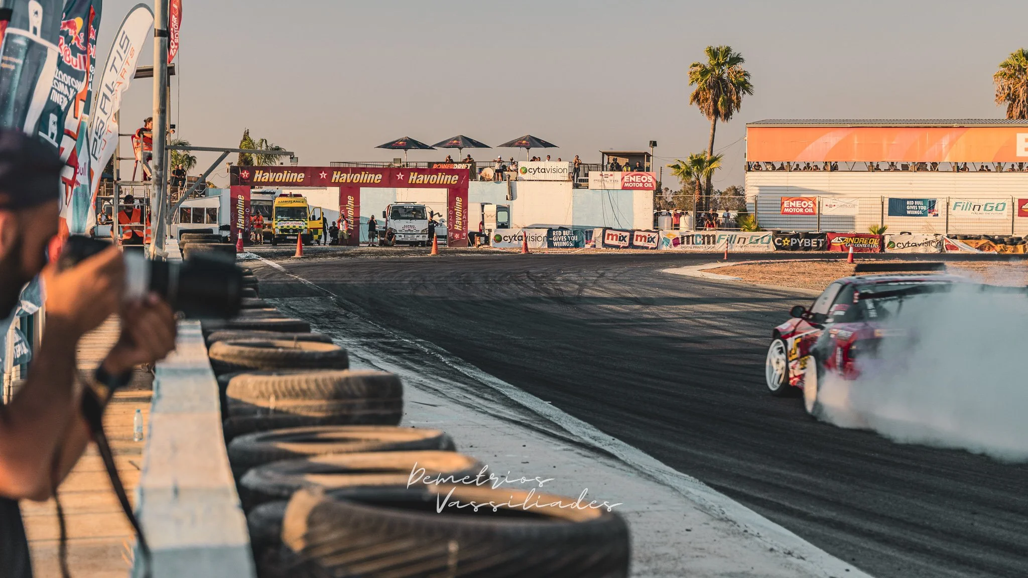 Drift car navigating a turn with sponsor banners and palm tree nearby.