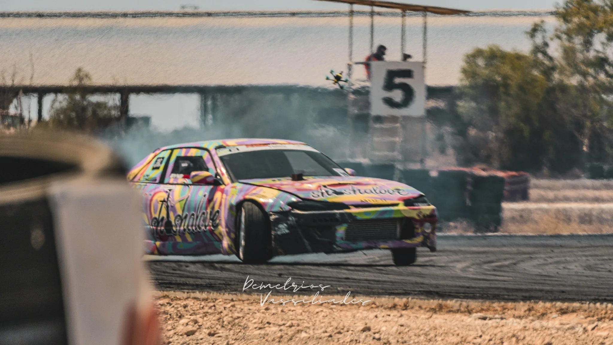 Colorful drift car with multicolored livery drifting past trackside barriers.