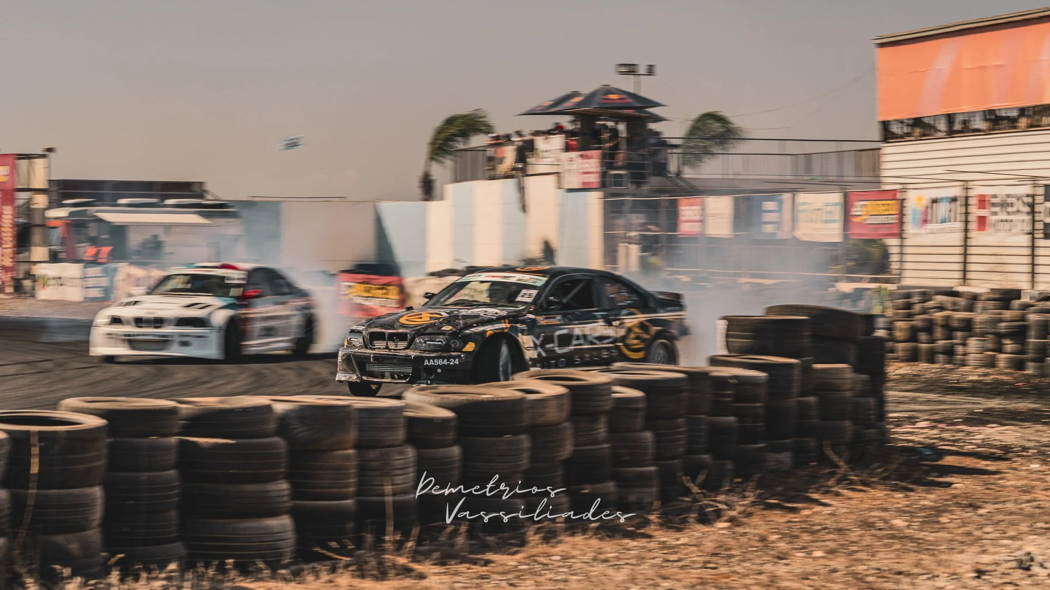 Drift cars battling on track surrounded by tire walls and smoke.