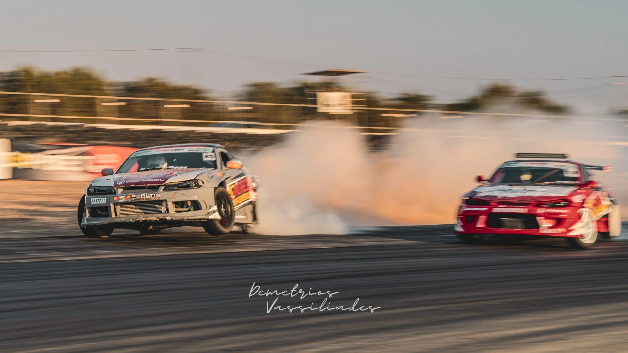 Silver drift car leading with heavy smoke as another car follows closely.