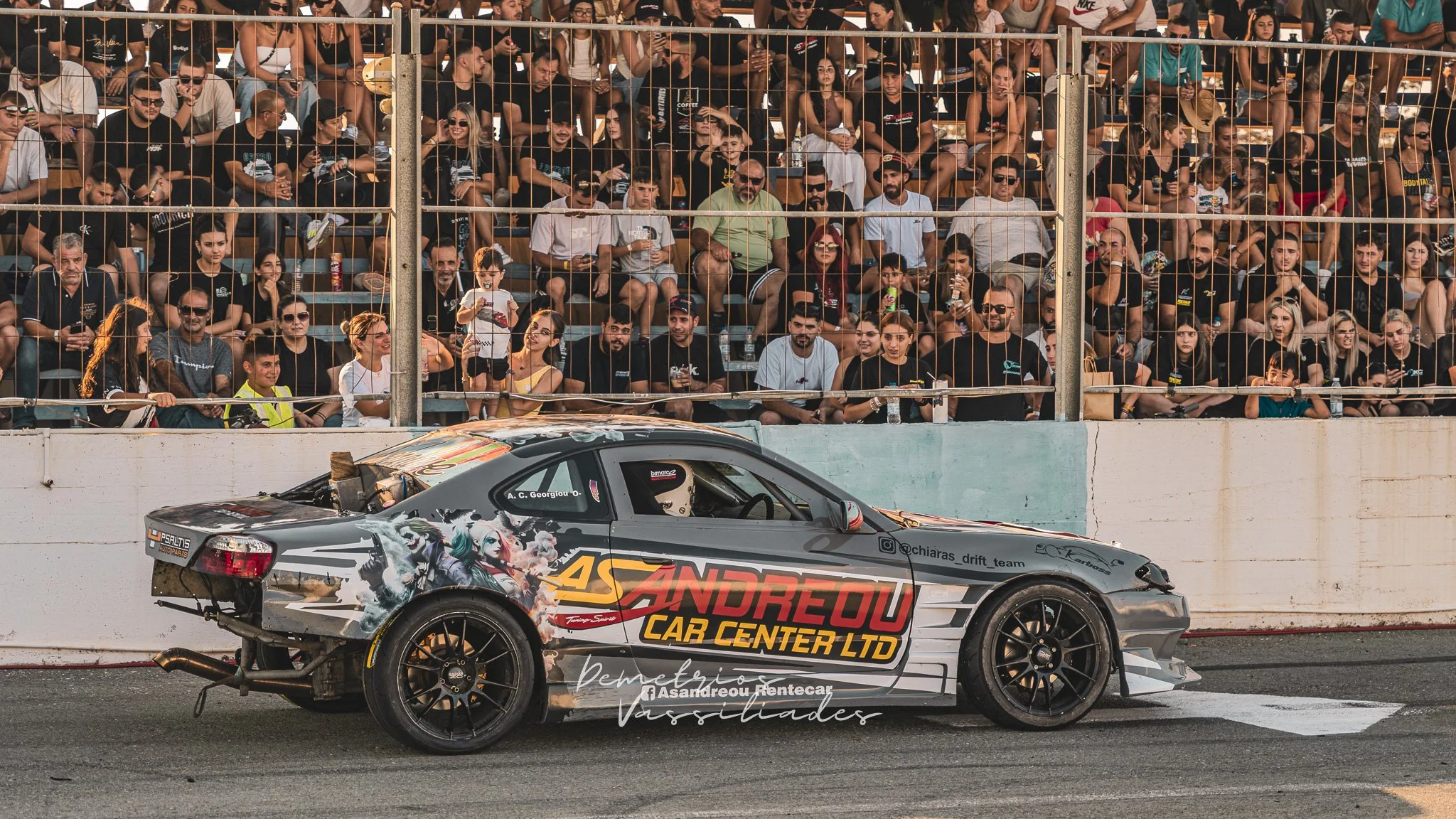 Drift car passing by a packed grandstand full of cheering spectators.