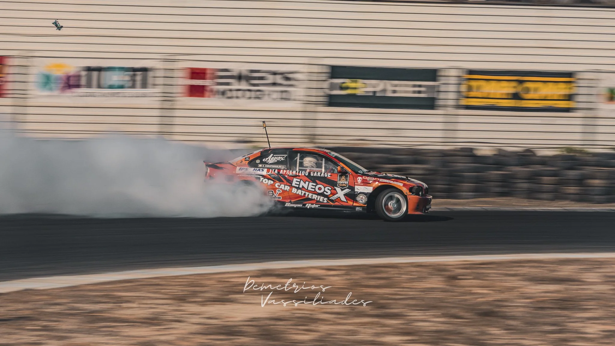 Orange drift car with ENEOS sponsorship sliding along the track in a smoky drift.