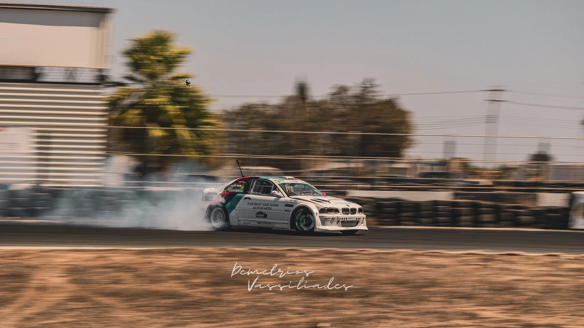 White BMW drift car drifting through a tight corner with smoke.