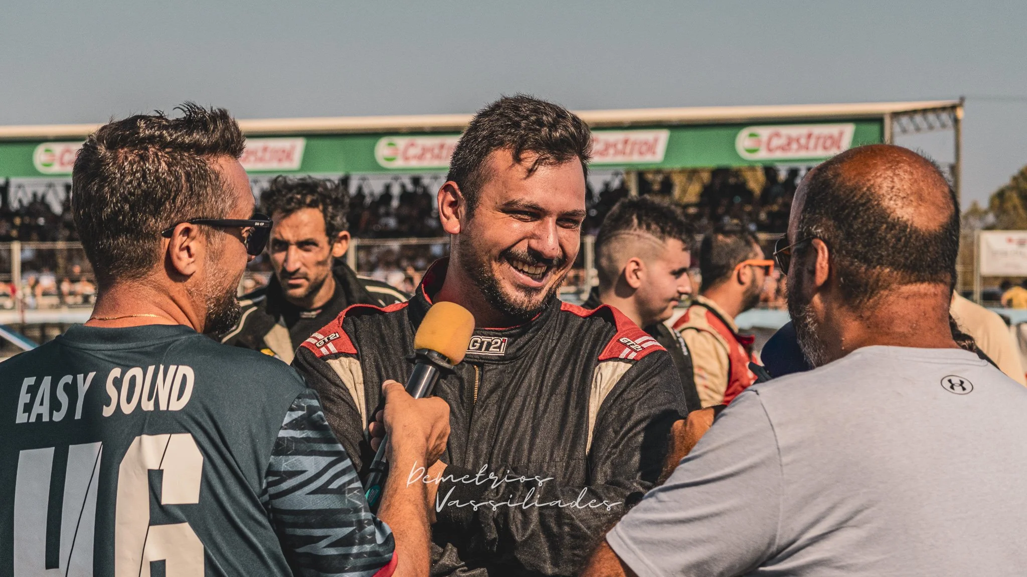 Drift driver smiling while giving an interview surrounded by media and fans.