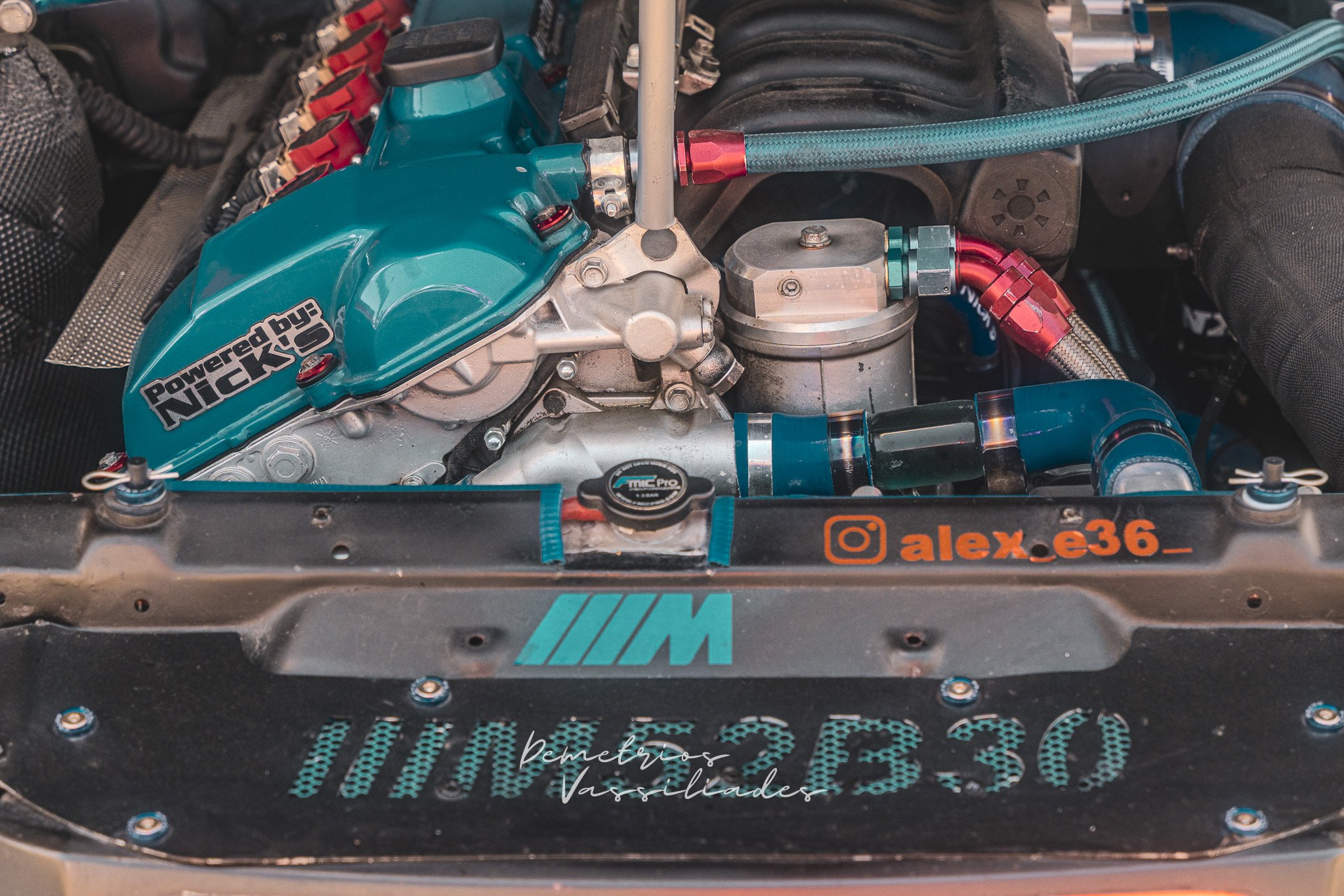 Close-up of a turquoise BMW drift car engine bay with performance parts.