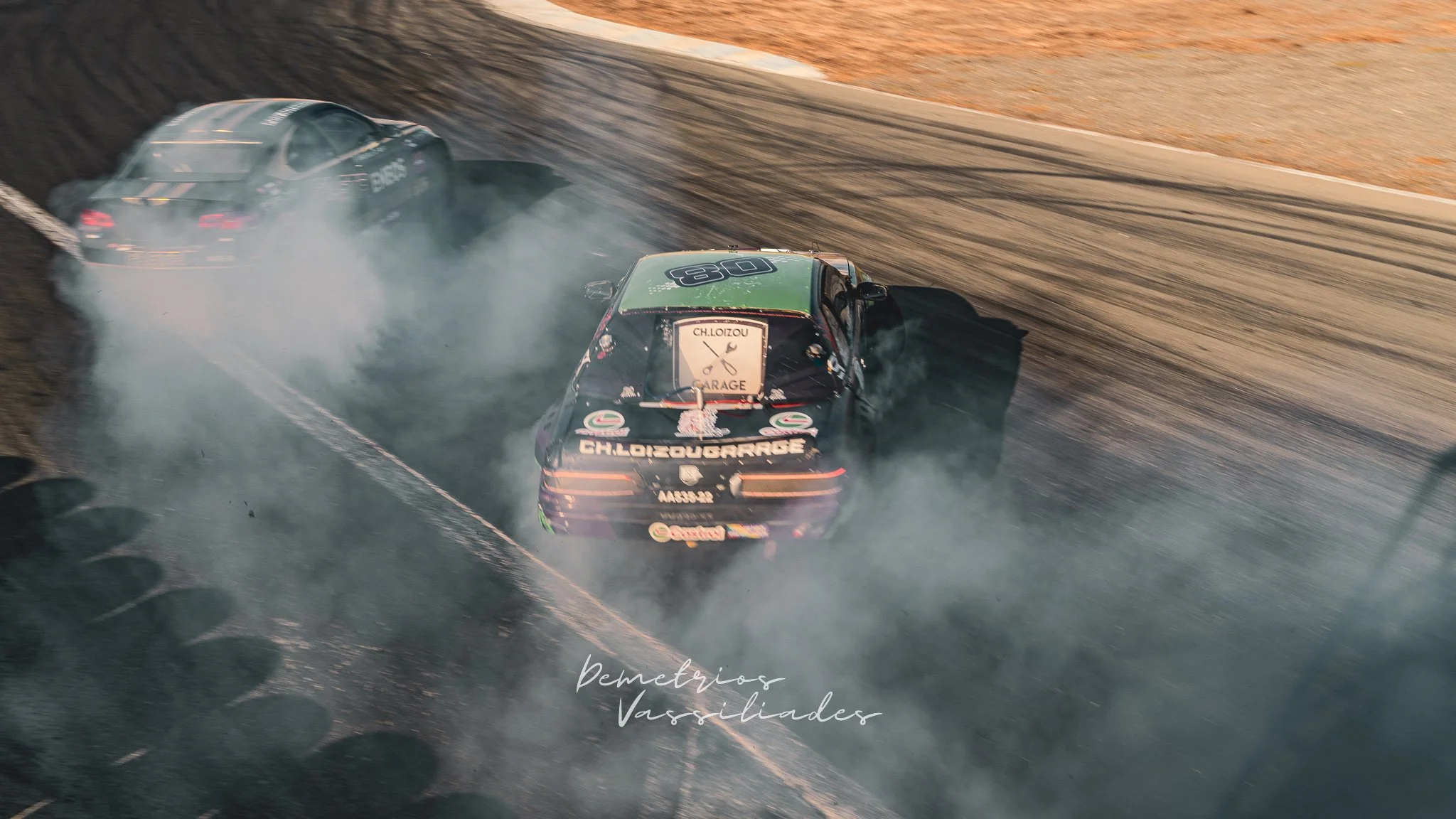 Black drift car spinning tires and producing thick smoke on track.