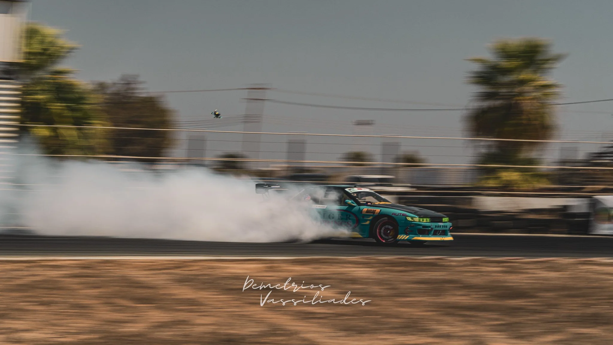 Green drift car in a fast drift leaving a cloud of tire smoke.