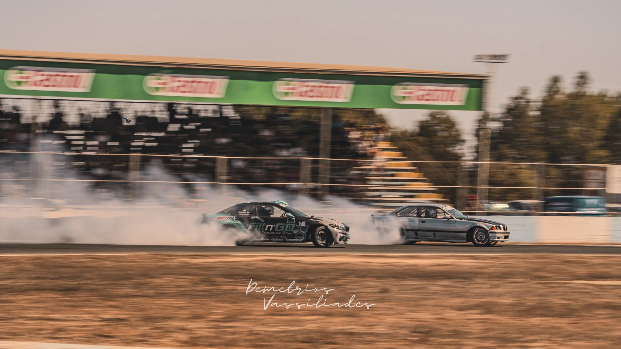 Two drift cars battling closely on track with tire smoke trailing behind.