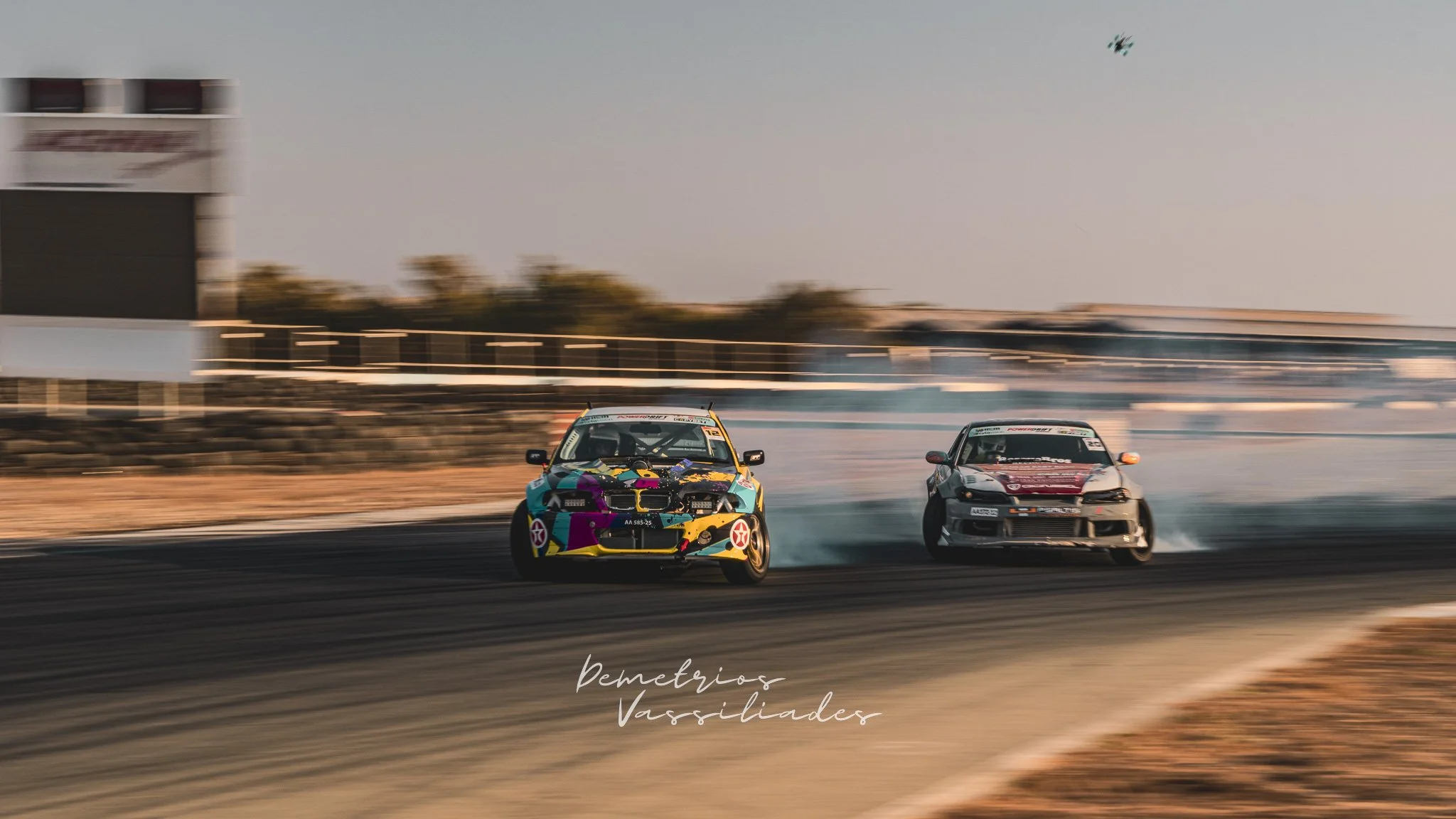 Grey drift car chasing a competitor mid-drift with heavy smoke.