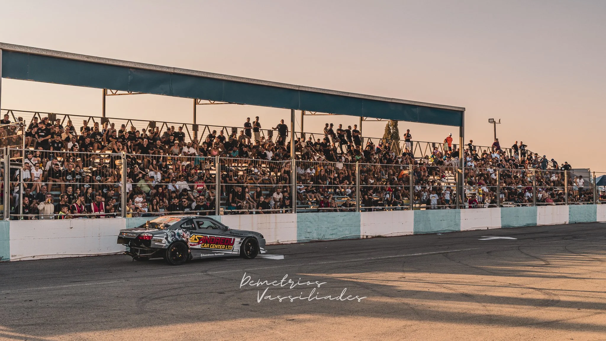 Drift car passing a grandstand packed with spectators at Achna Speedway.