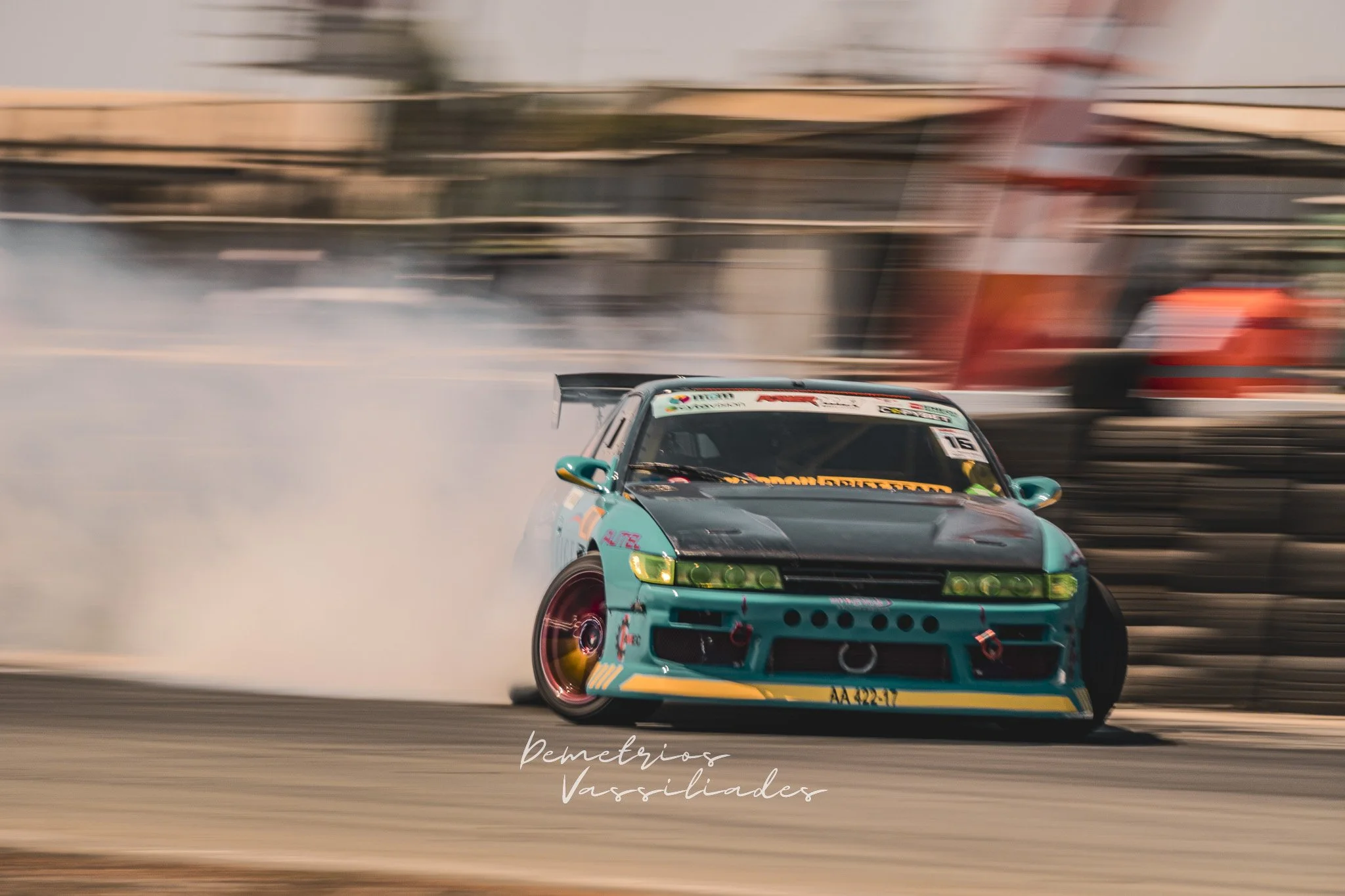Teal drift car sliding aggressively with tires smoking on exit.