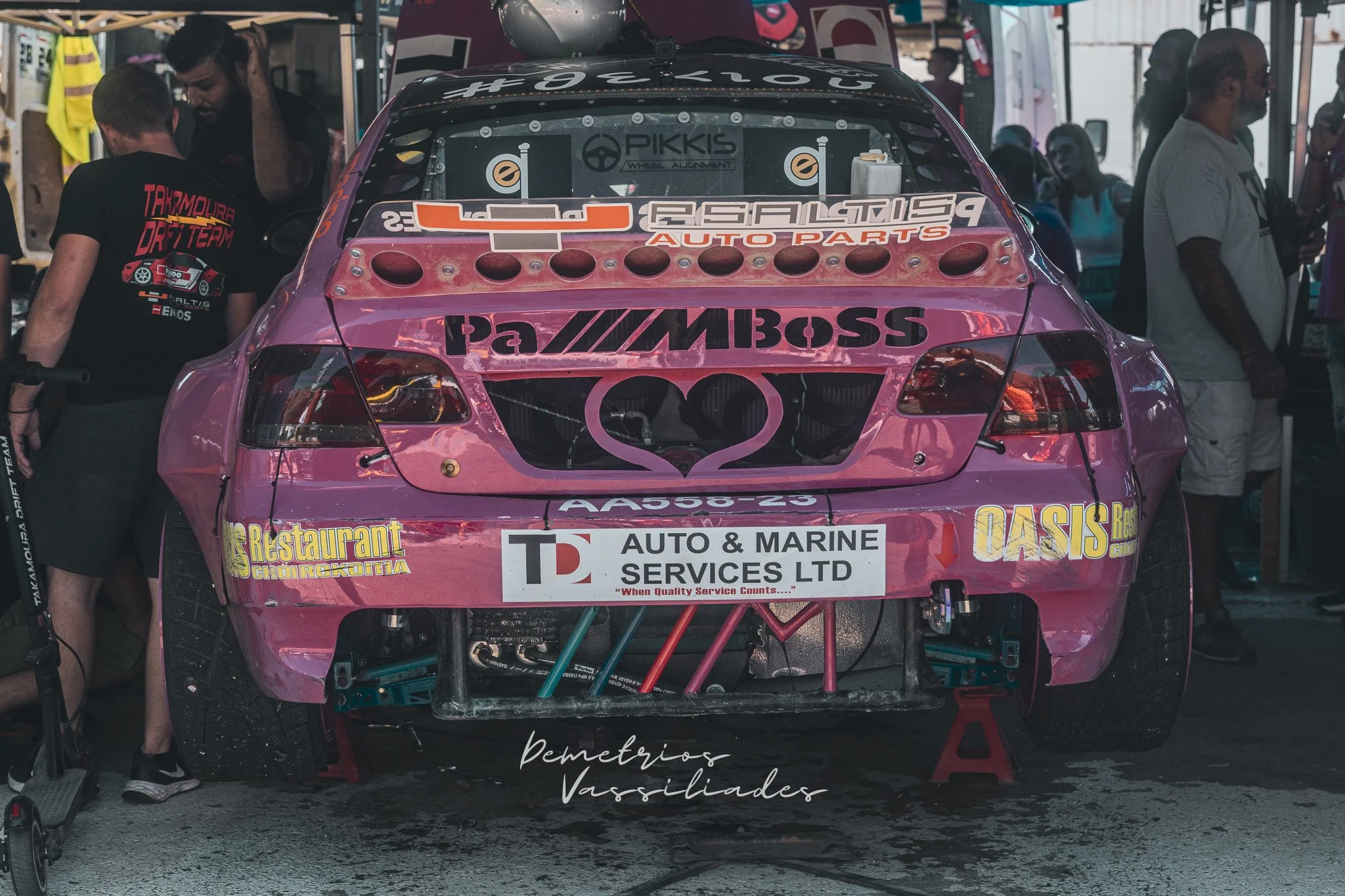 Rear view of a pink drift car with sponsor decals parked in the paddock.