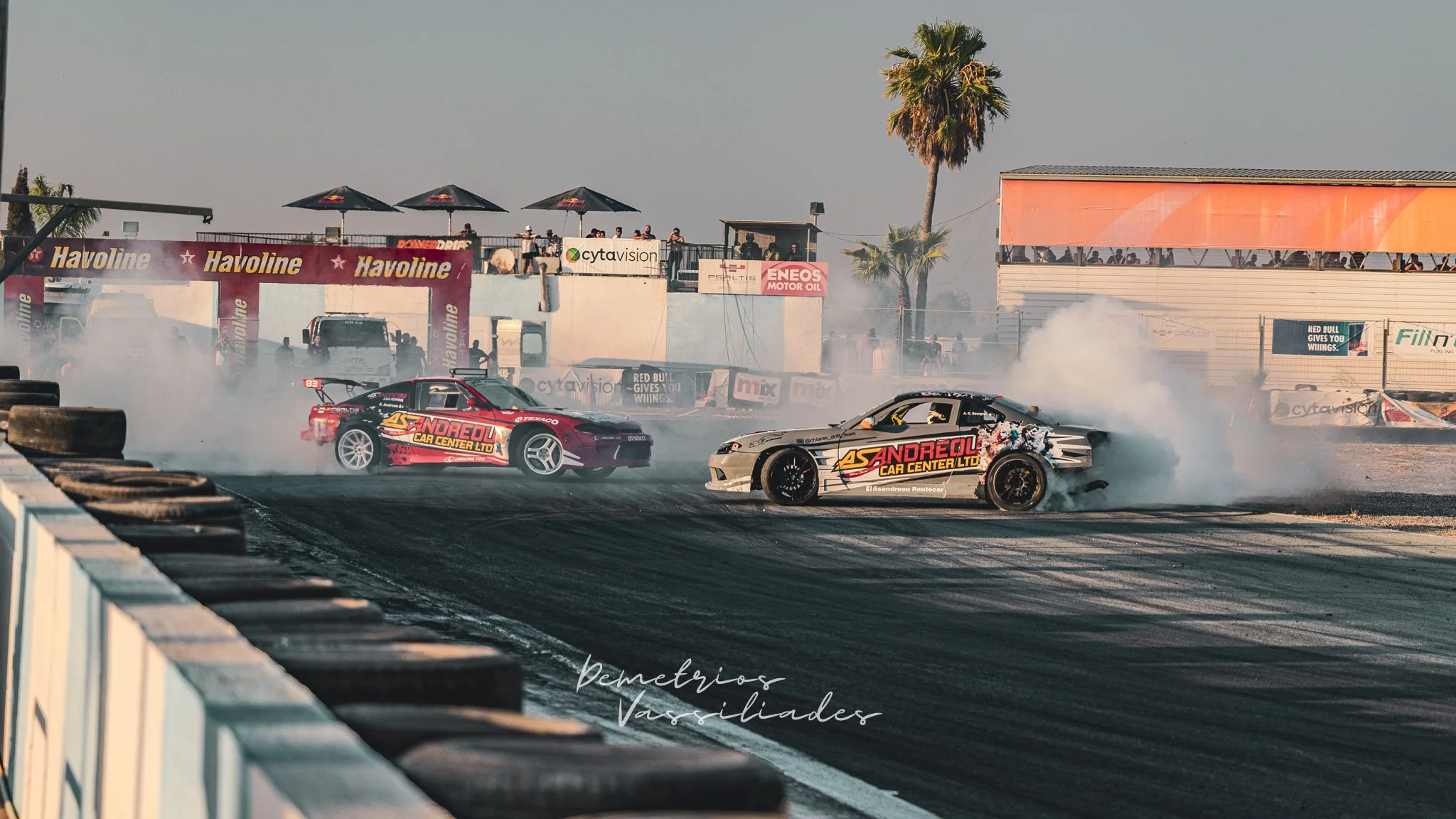 Two drift cars competing side by side with palm trees in the background.