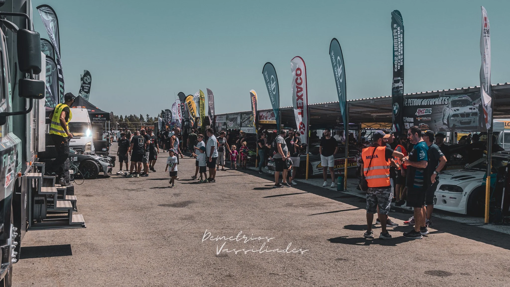 Spectators walking past sponsor tents and flags at Achna Speedway during the drift event.