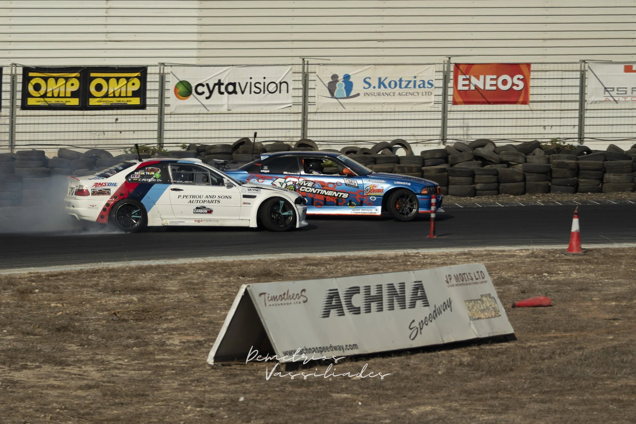 Two drift cars lined up on track near an Achna Speedway barrier.