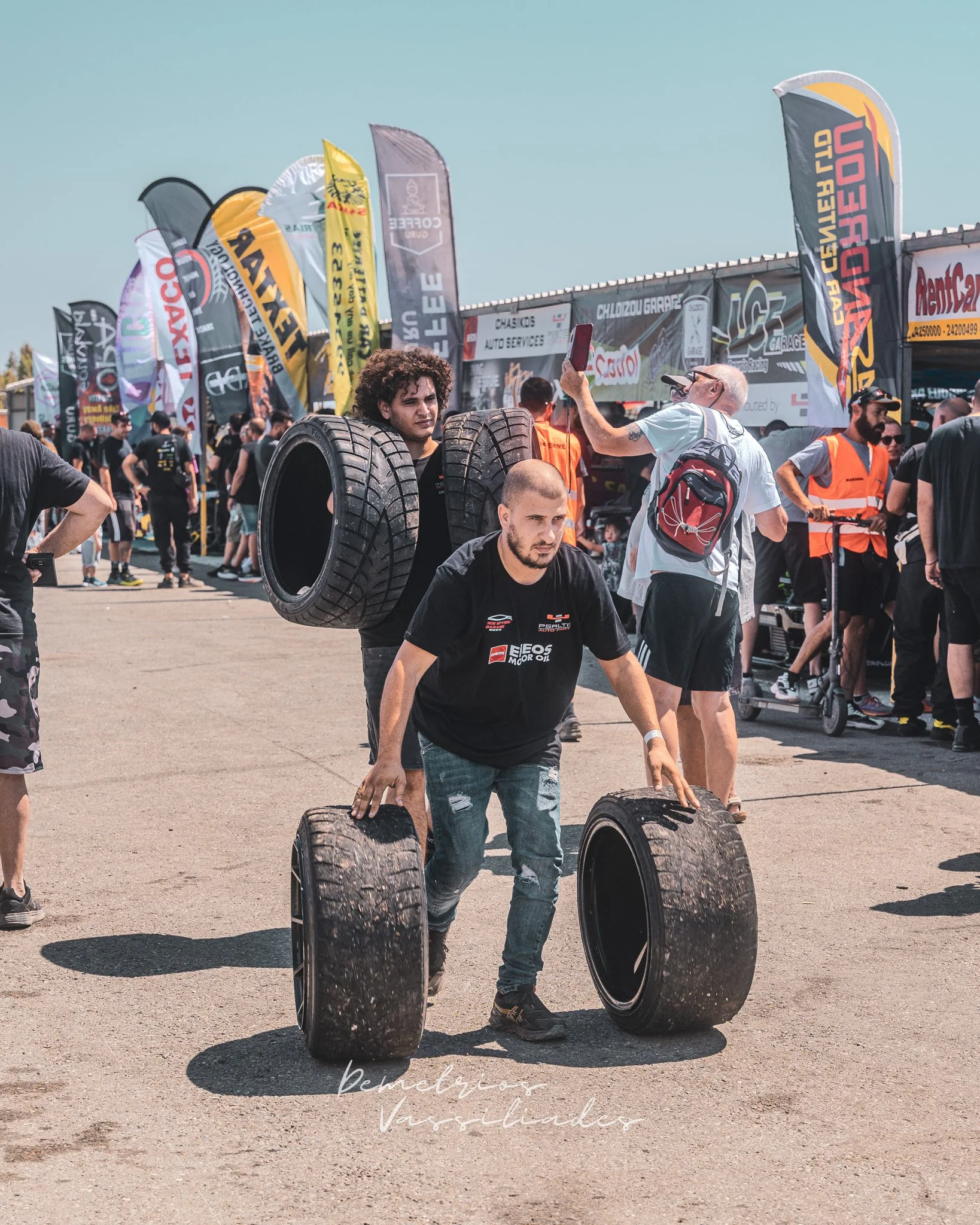 Two men carrying stacked tires through the paddock at Cyprus Drift Championship.