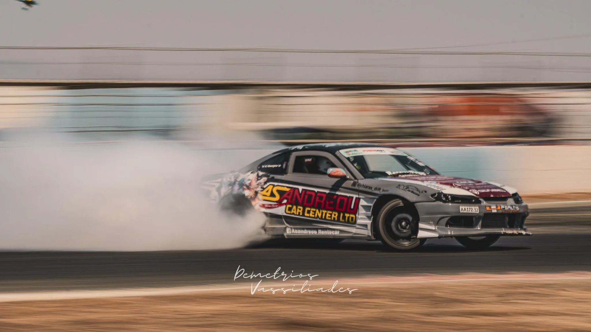 Silver drift car sliding sideways with smoke trailing behind.