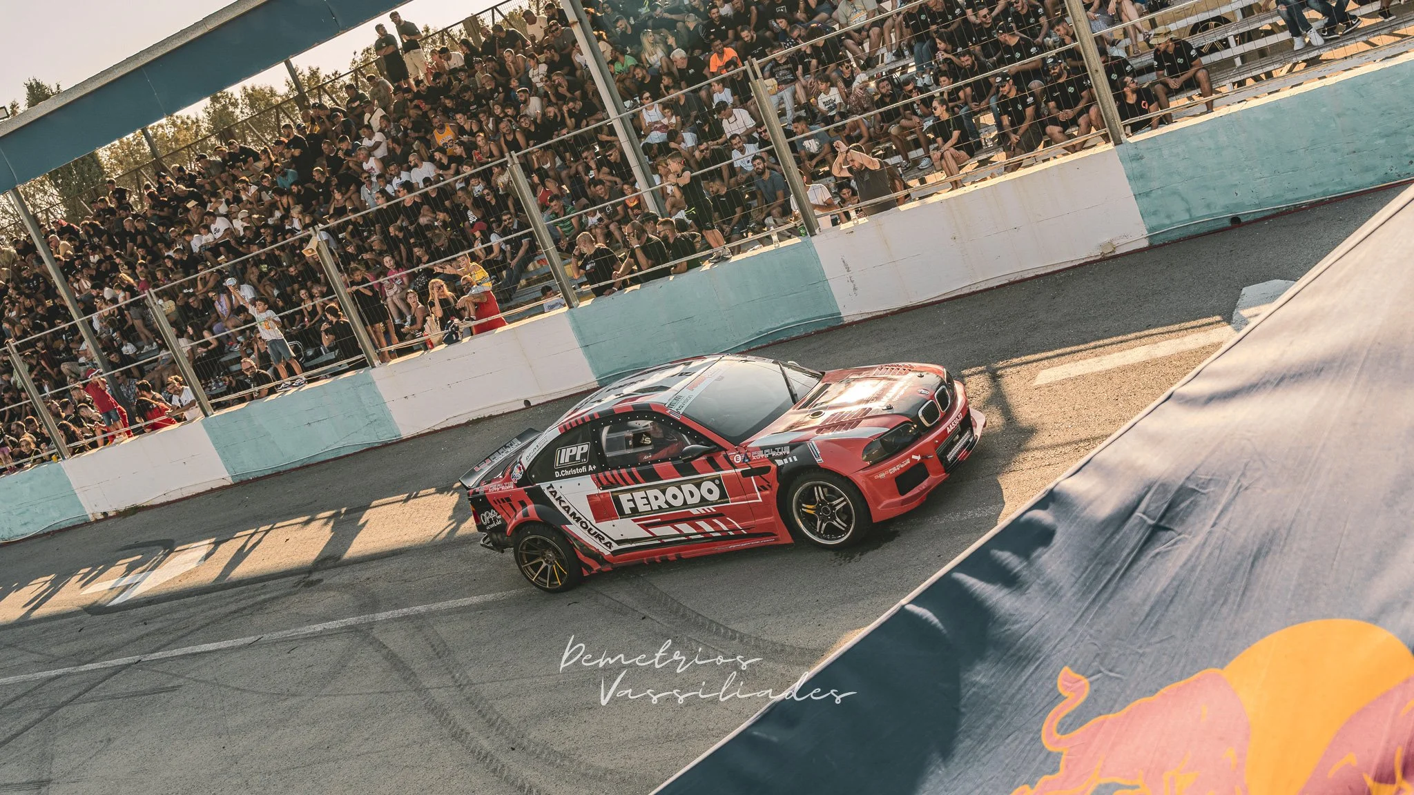 Red drift car with Ferodo branding sliding past cheering spectators.
