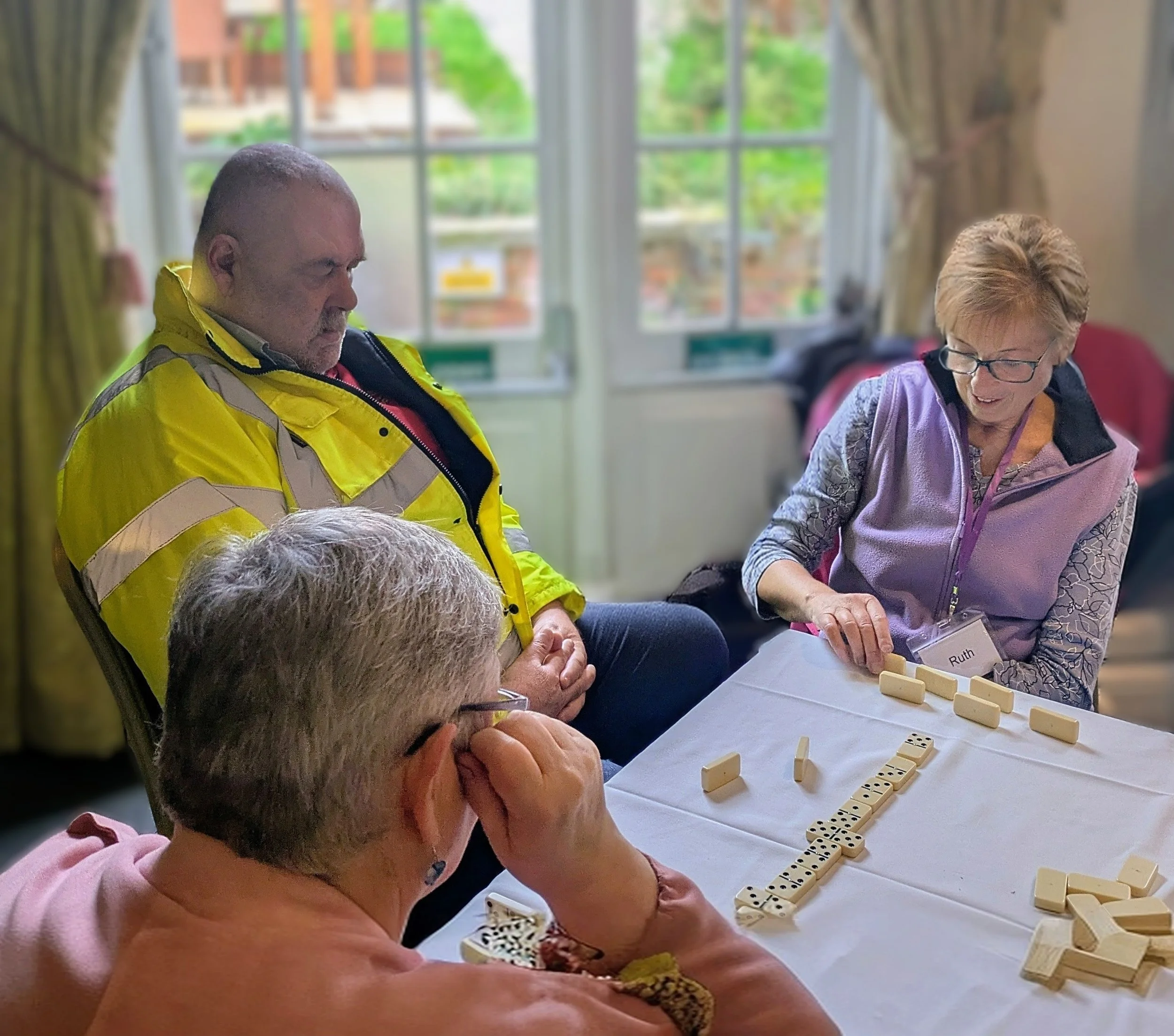 Two Speakability members and a volunteer playing a game of dominoes at a meeting.