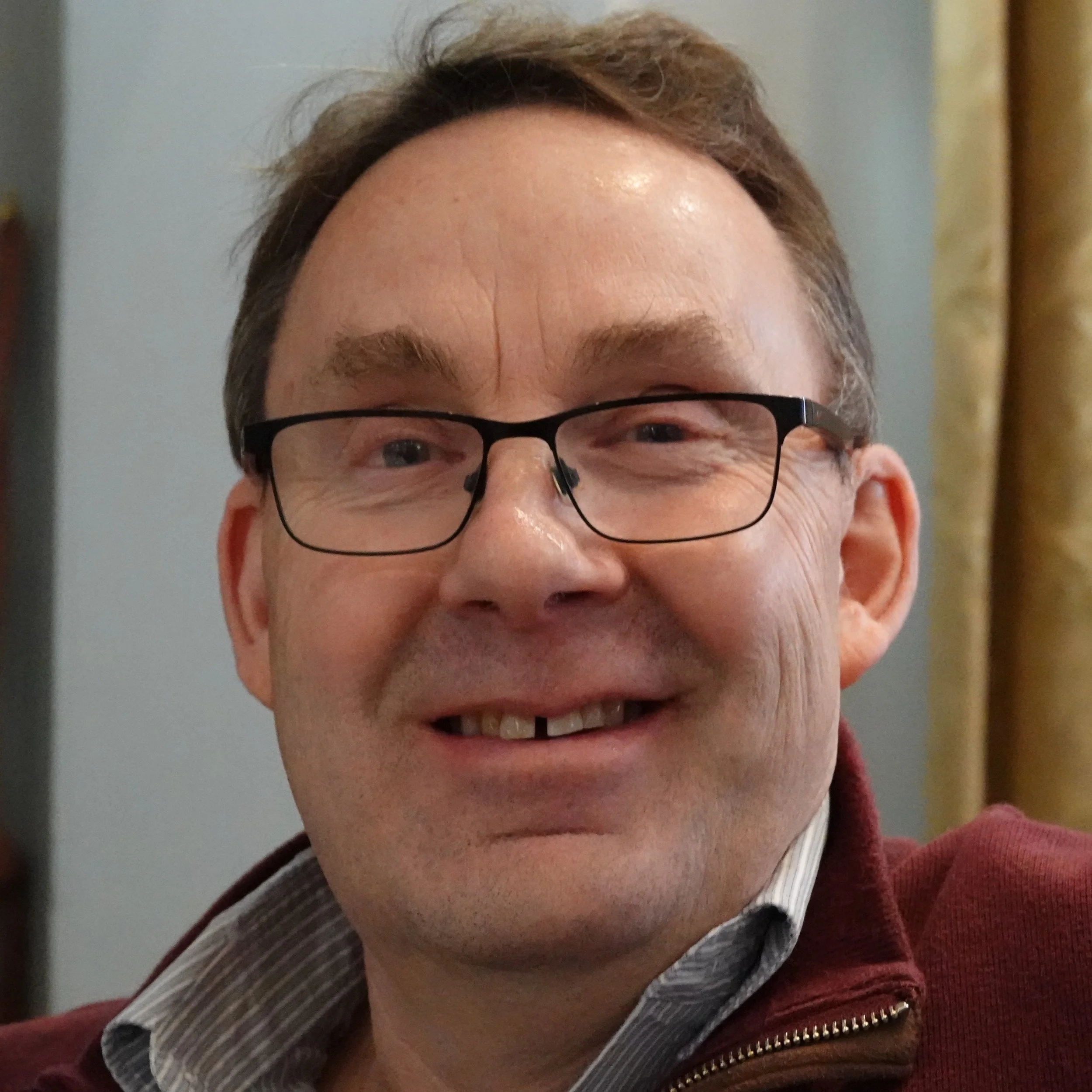 Close-up of a smiling man wearing glasses, a striped shirt, and a maroon jacket at a Speakability meeting in Newbury