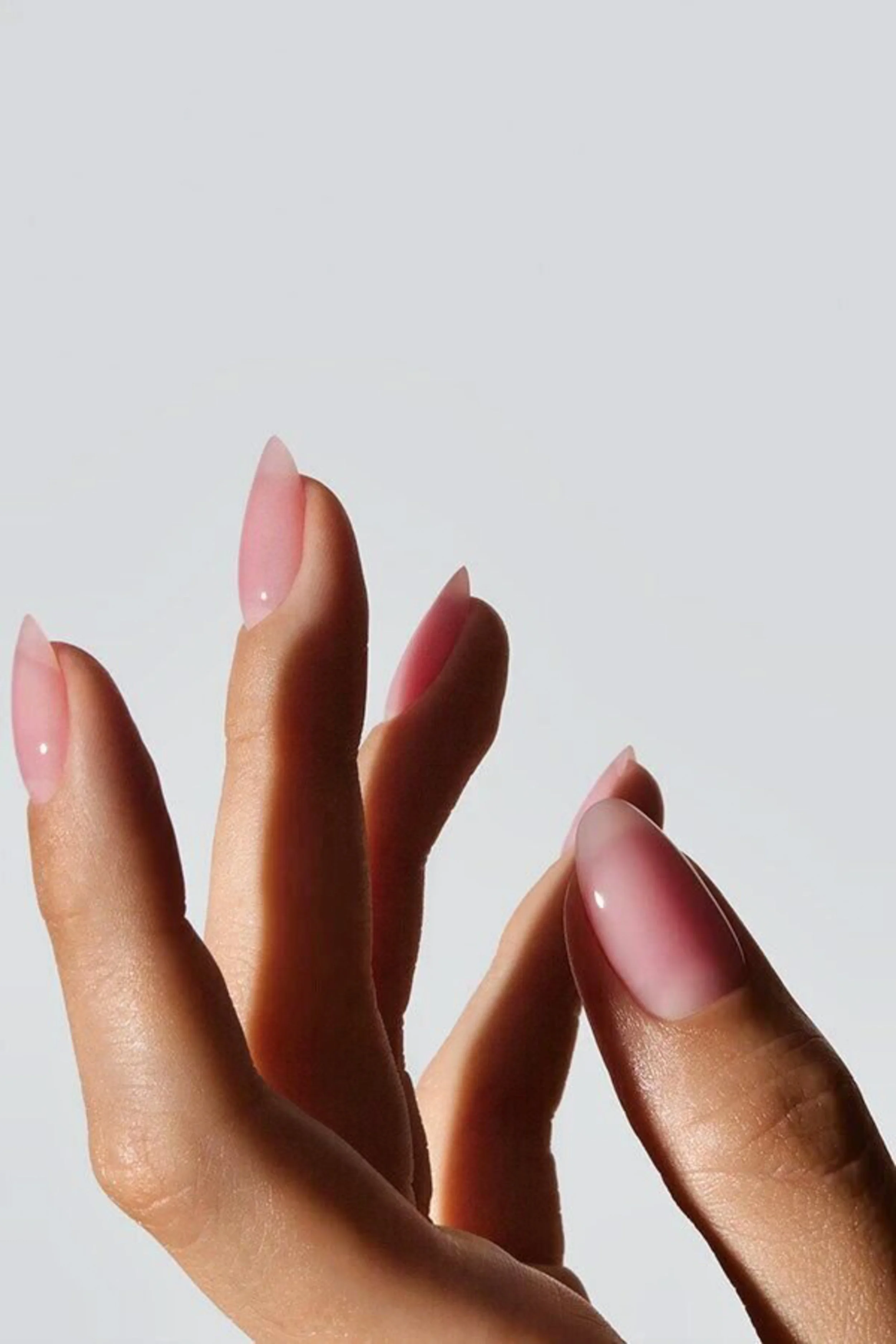 Close-up of a hand with brown skin and manicured nails painted in a shiny, neutral color, wearing a brown sweater with a ribbed cuff.