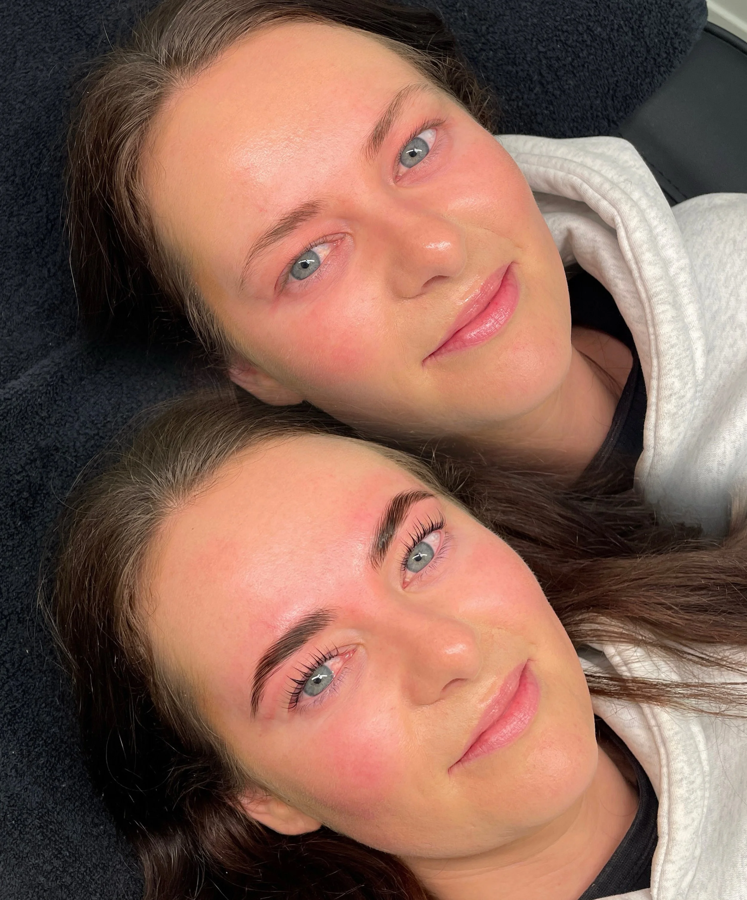 Close-up of a young woman lying down with her head on a black surface, with clear skin, blue eyes, and brown hair, wearing a white hoodie.