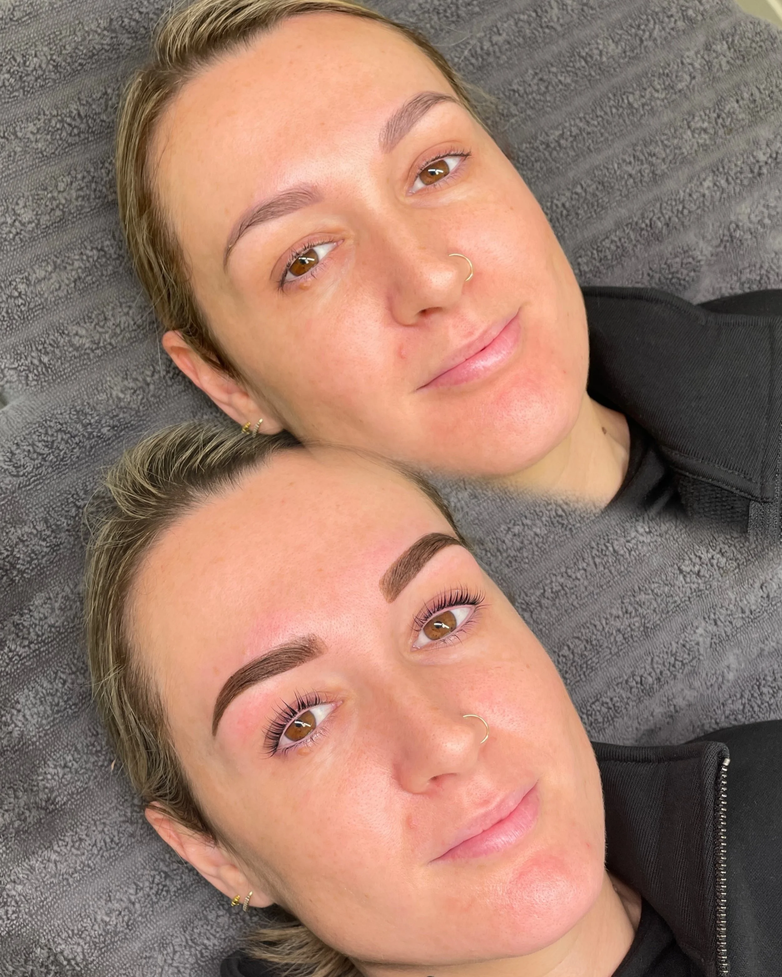 Close-up of a woman's face with short light brown hair, brown eyes, and freckles, lying on a textured gray surface, wearing a black top and gold jewelry.