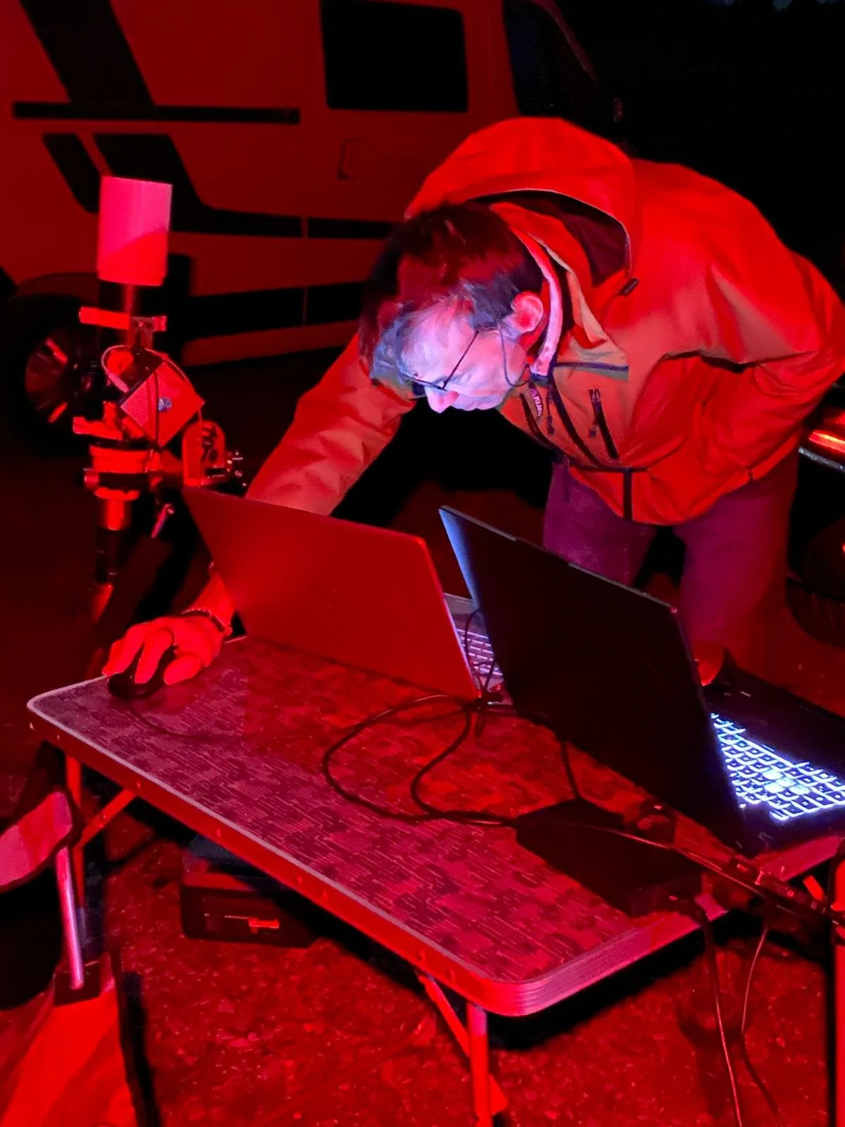 Grand bâtiment en bois avec balcon, situé dans un environnement naturel avec arbres et voiture à l'avant