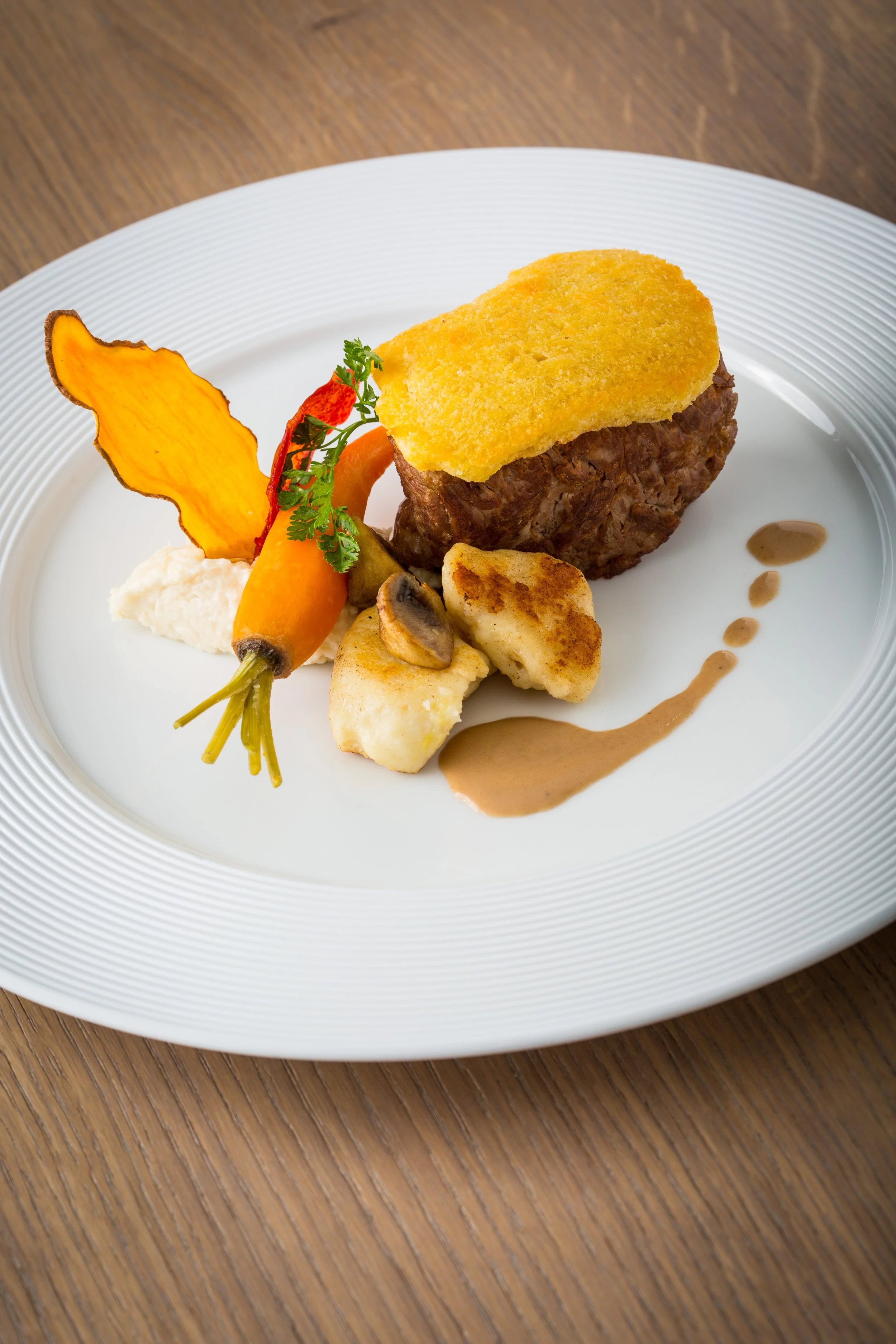 Assiette gastronomique avec un morceau de viande, une couche de purée, légumes grillés, une sauce, et une fine tranche de courge