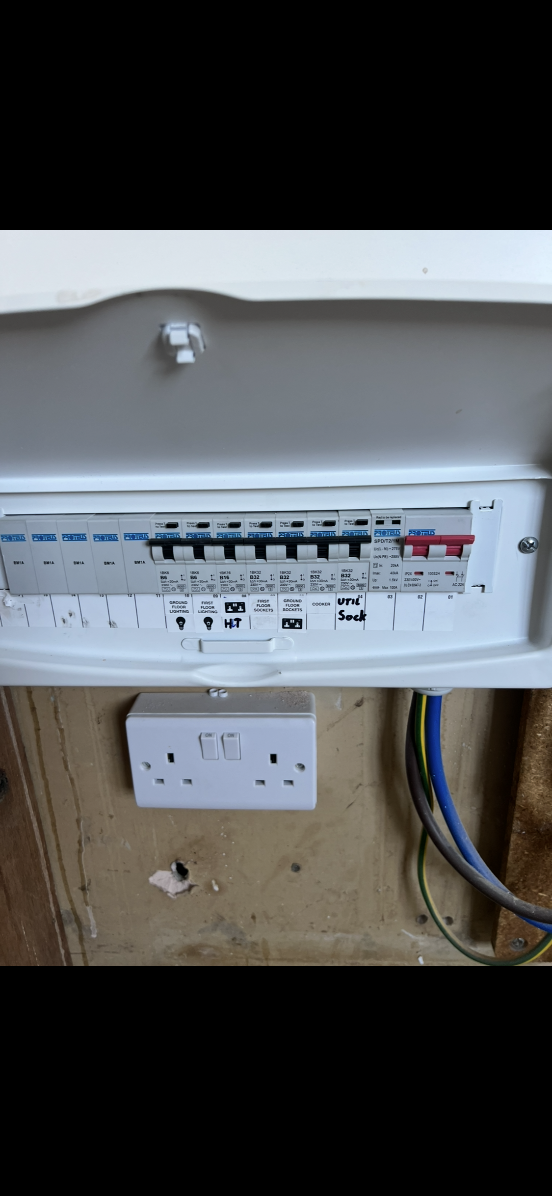 Electric circuit breaker panel with wiring and a nearby outlet, installed on a wall.