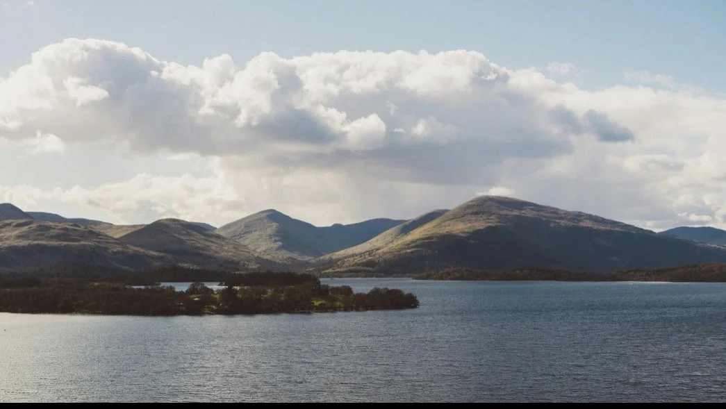 A scenic view of a lake with mountains in the background under a partly cloudy sky.