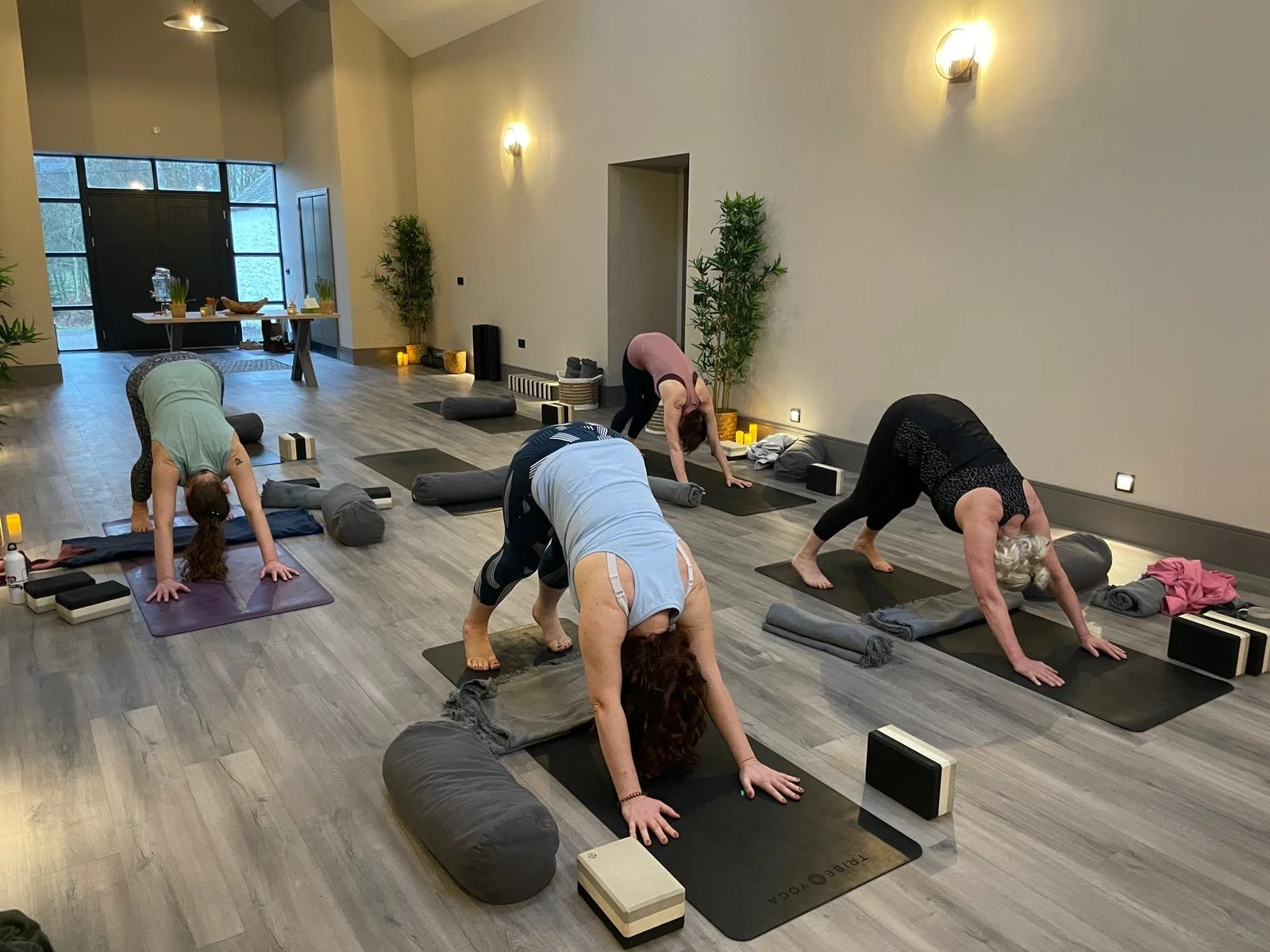 People practicing yoga in a spacious, well-lit room with mats, cushions, and candles.