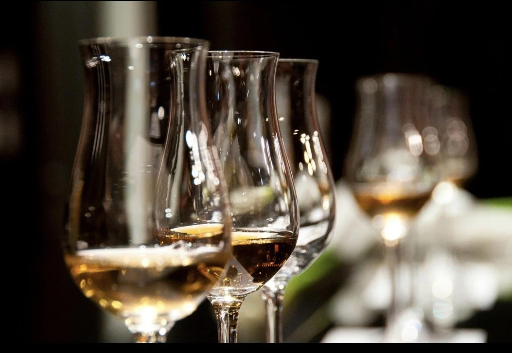 Four wine glasses with white wine, arranged in a row with focus on the first glass, dimly lit background.