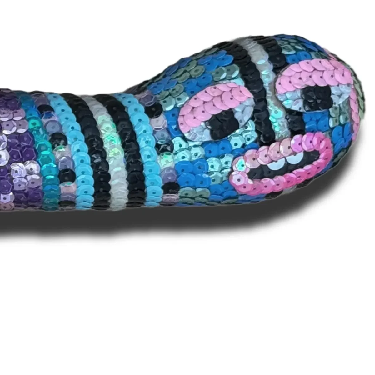 Close-up of a snake-shaped object covered in multicolored sequins, with a pattern resembling a snake's face, on a white background.