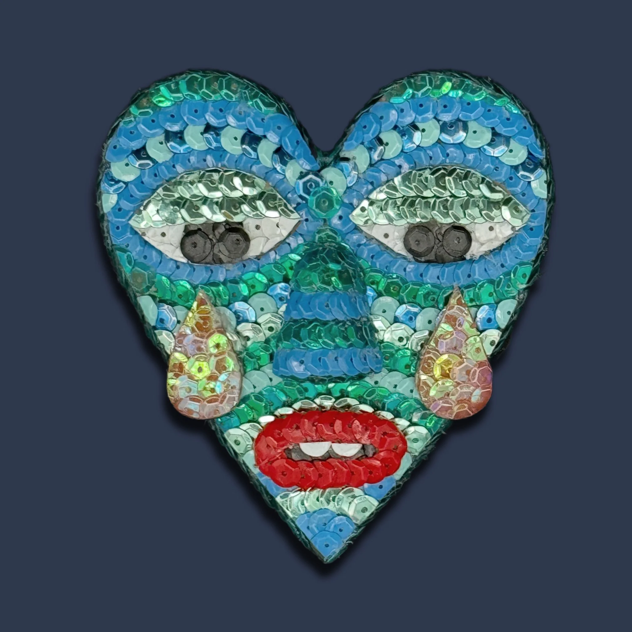 Heart-shaped mosaic art featuring a crying face with teardrops, styled with colorful sequins and beads.